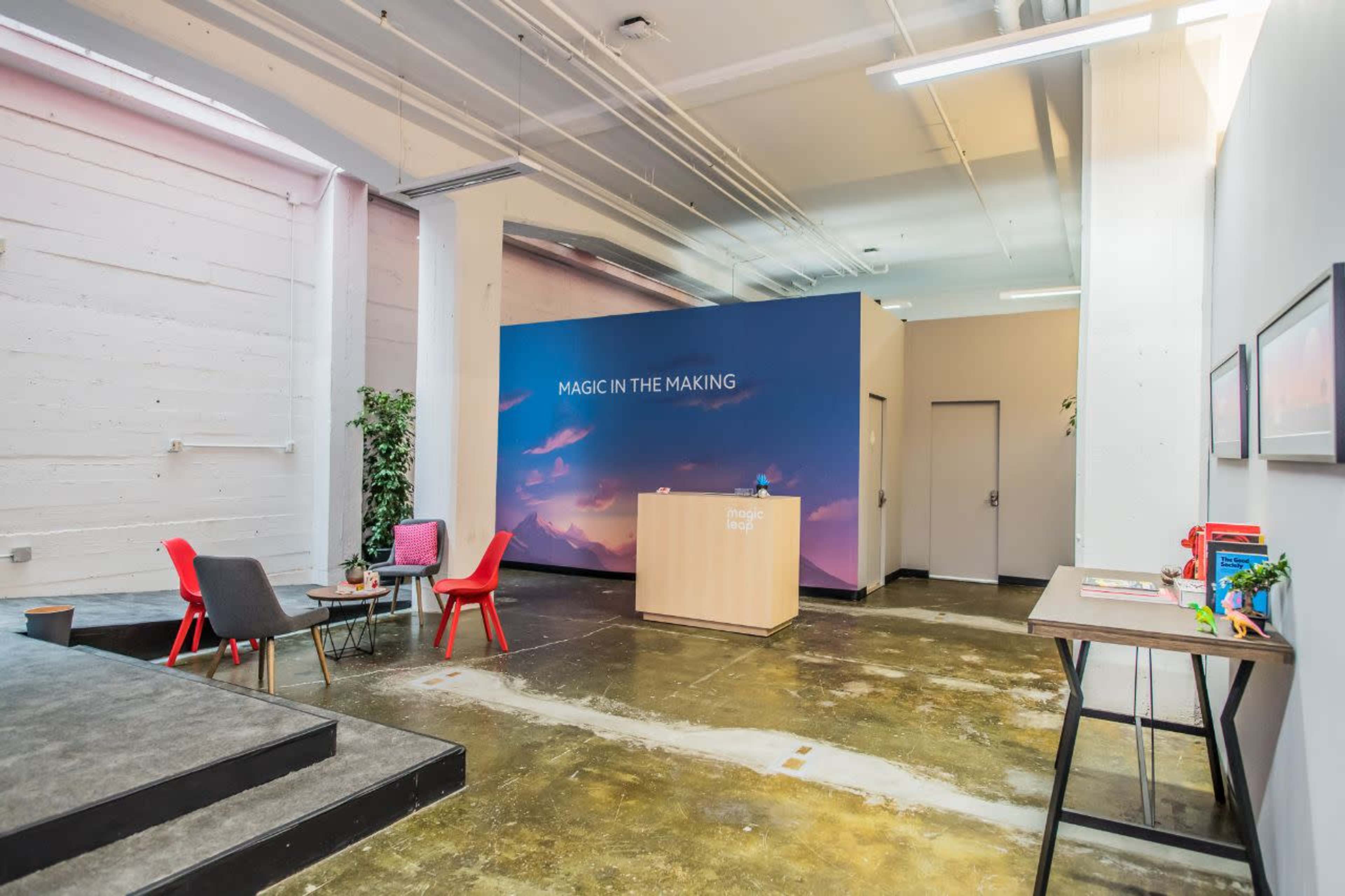 A modern reception area with a desk, two chairs, and a large wall mural that reads "MAGIC IN THE MAKING."