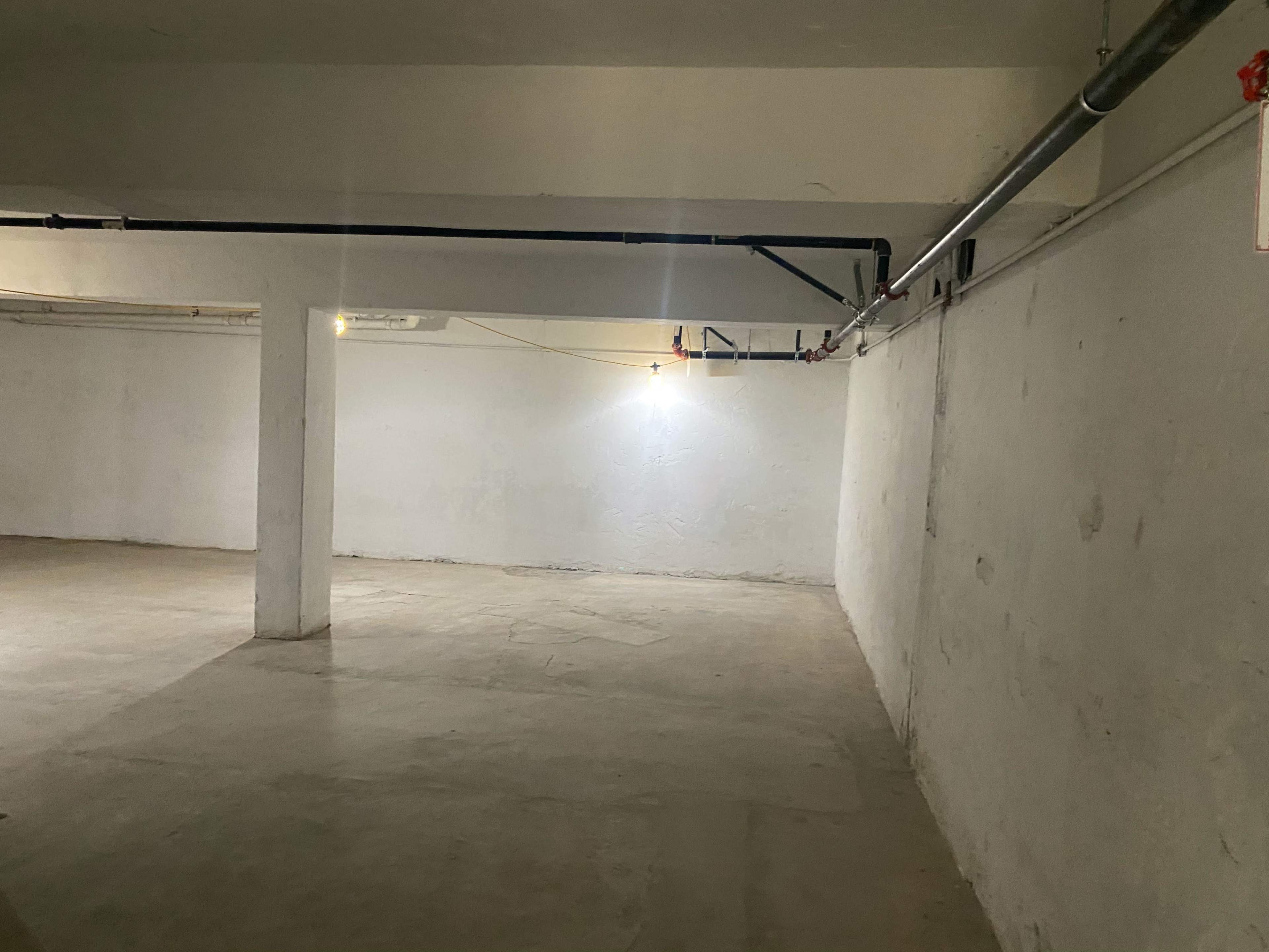 A spacious, empty basement with bare concrete floors and exposed pipes along the ceiling.