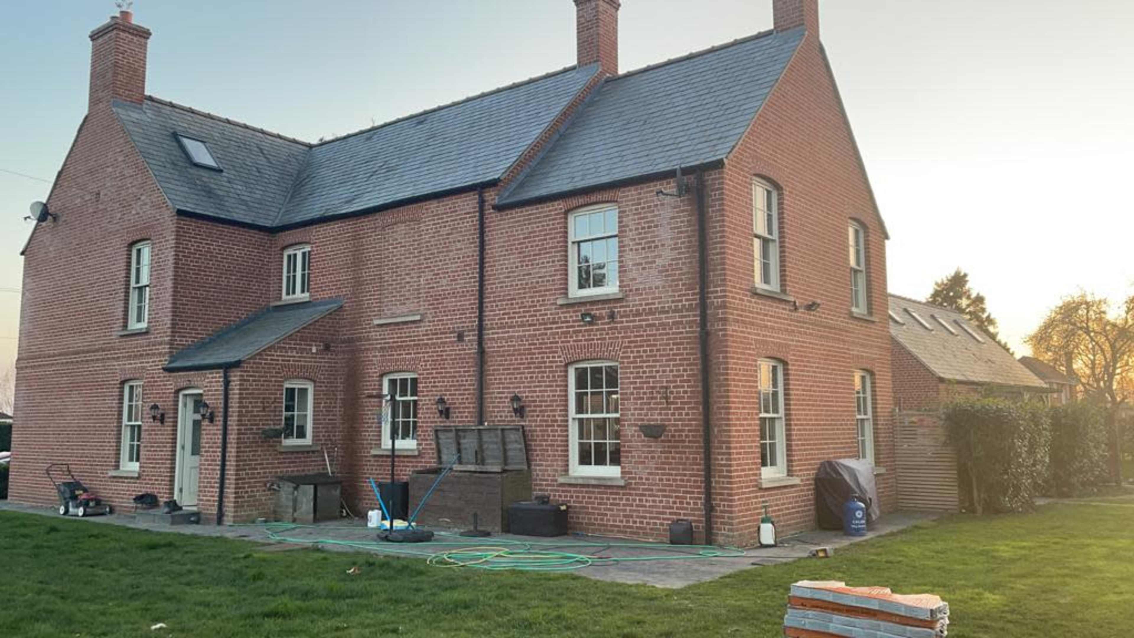 A two-story brick house with multiple windows, a grassy yard, and various tools and equipment nearby.