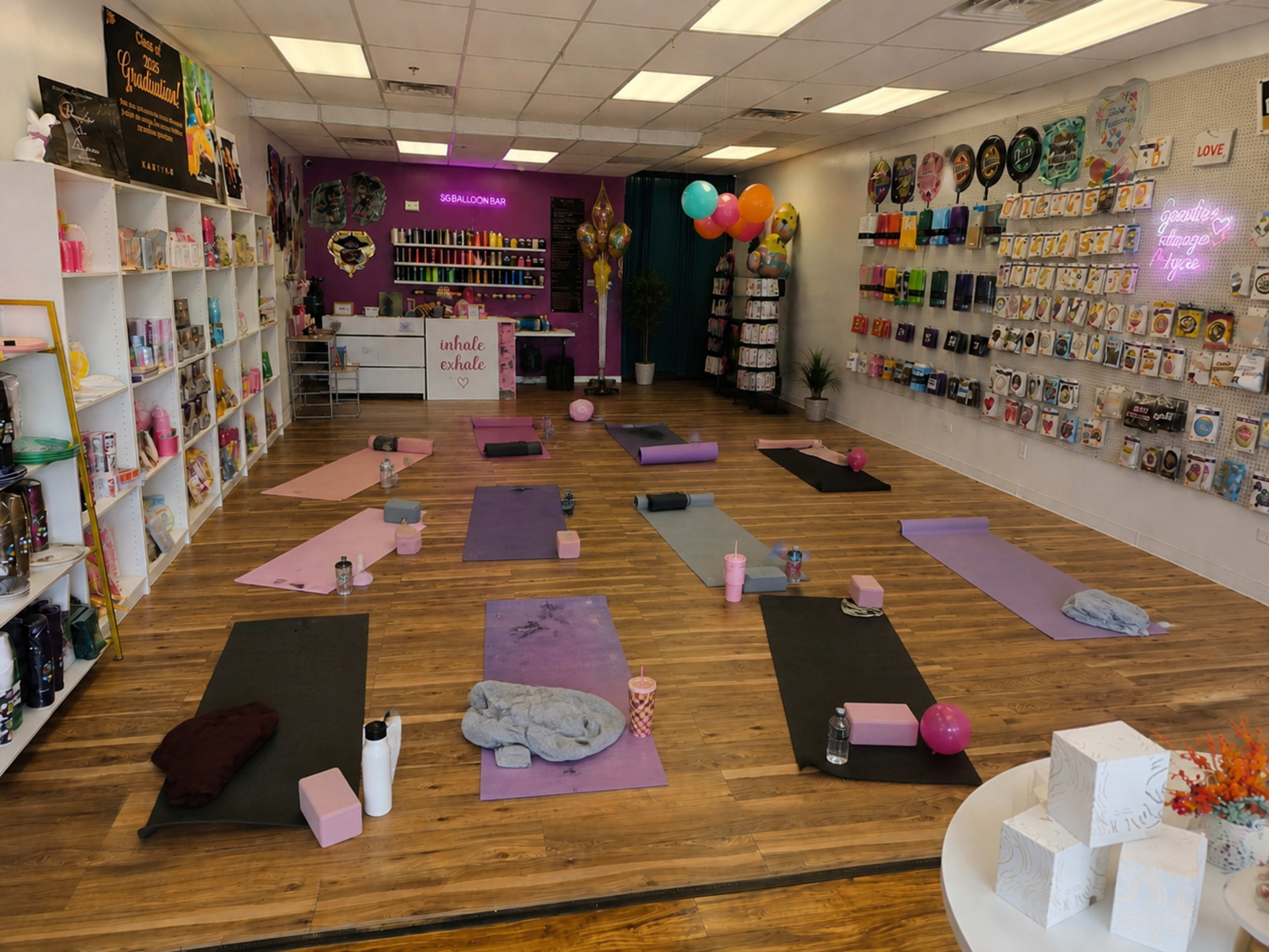 The image shows a yoga studio set up with multiple yoga mats arranged on a wooden floor, surrounded by colorful decor and various props for classes.