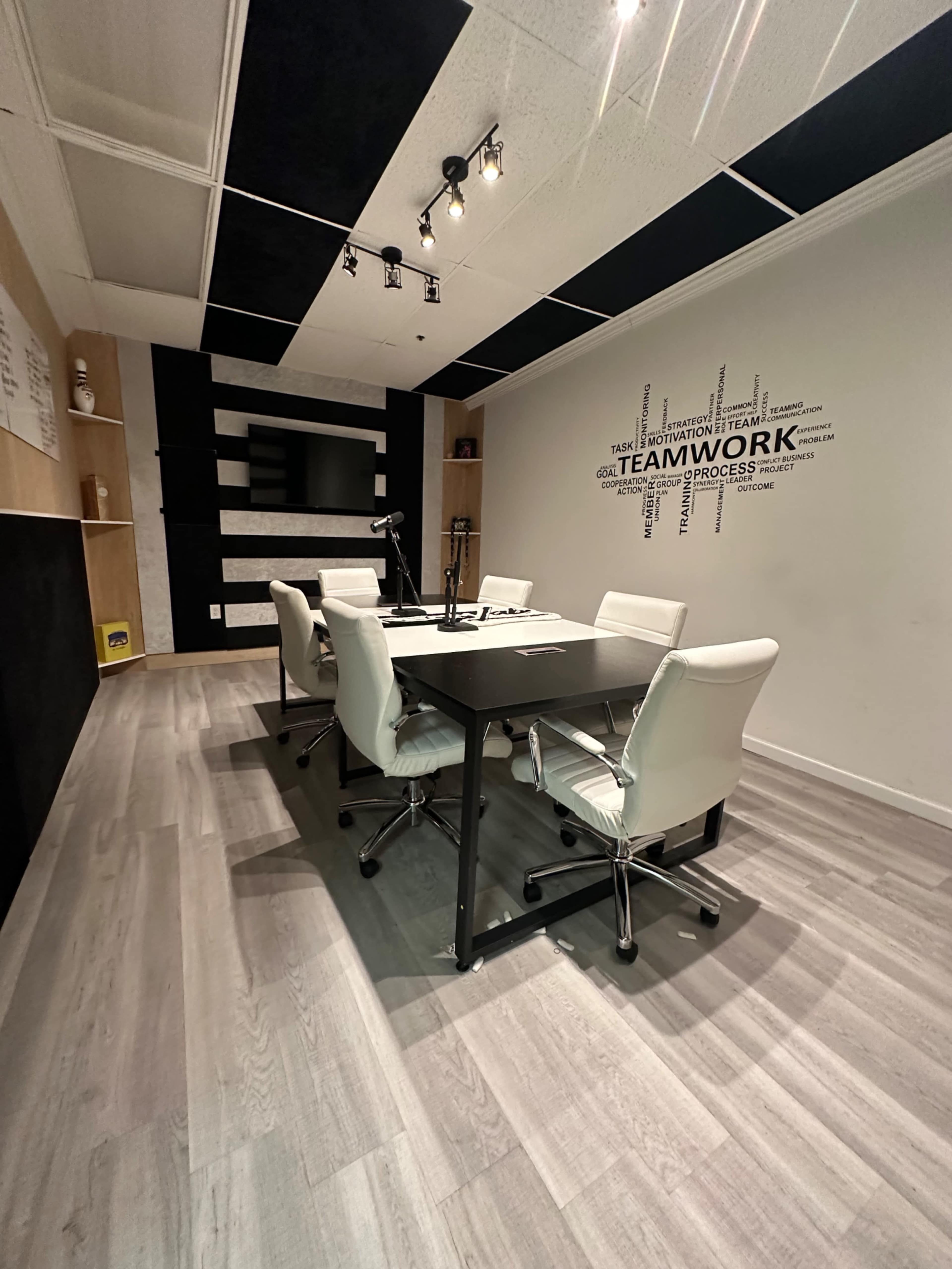 A modern conference room with a black and white color scheme, featuring a rectangular table surrounded by white chairs and a wall decorated with the word "TEAMWORK."