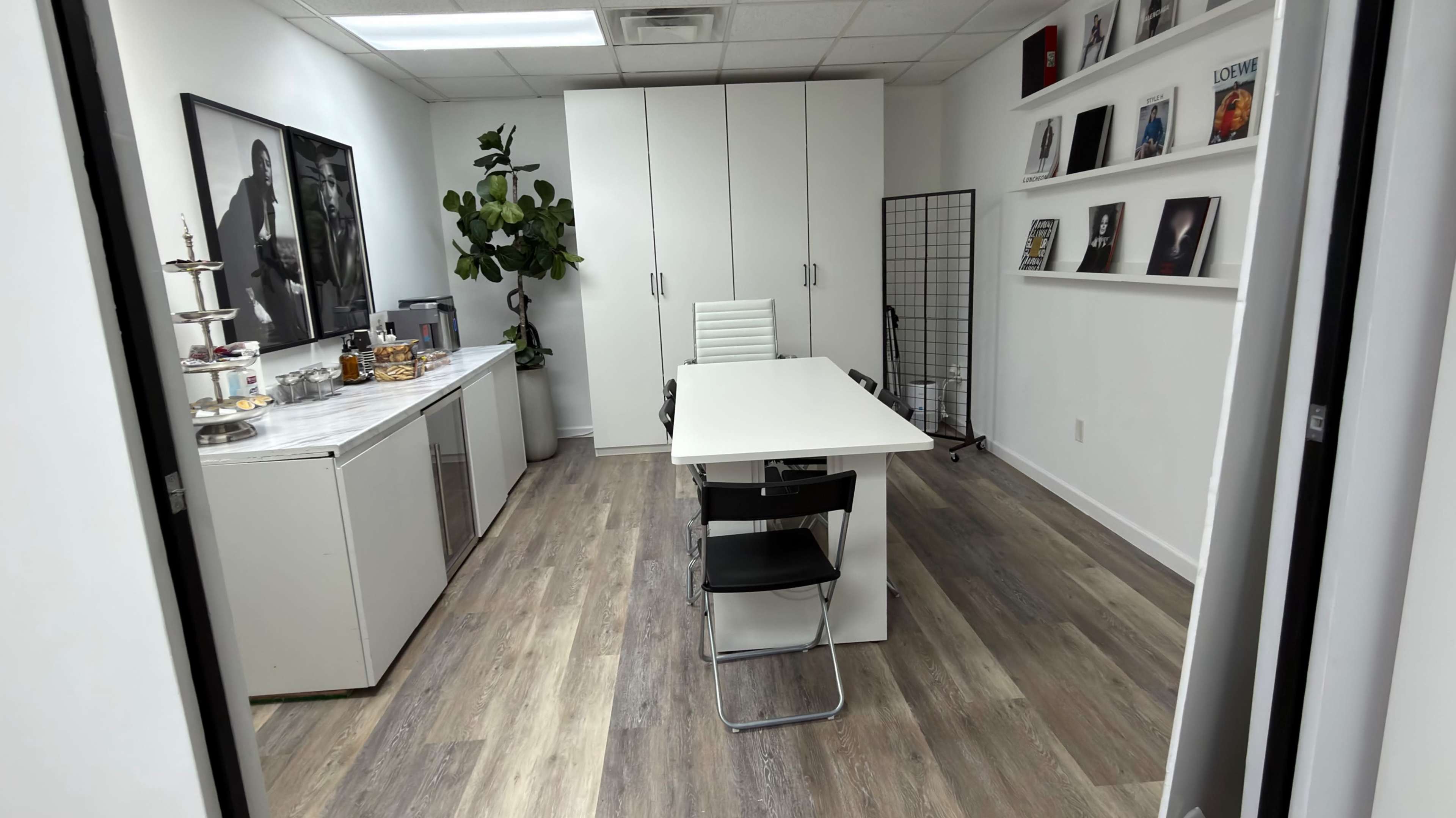 The image shows a modern office space with a white table and chairs, a large cabinet, and shelves displaying various items.