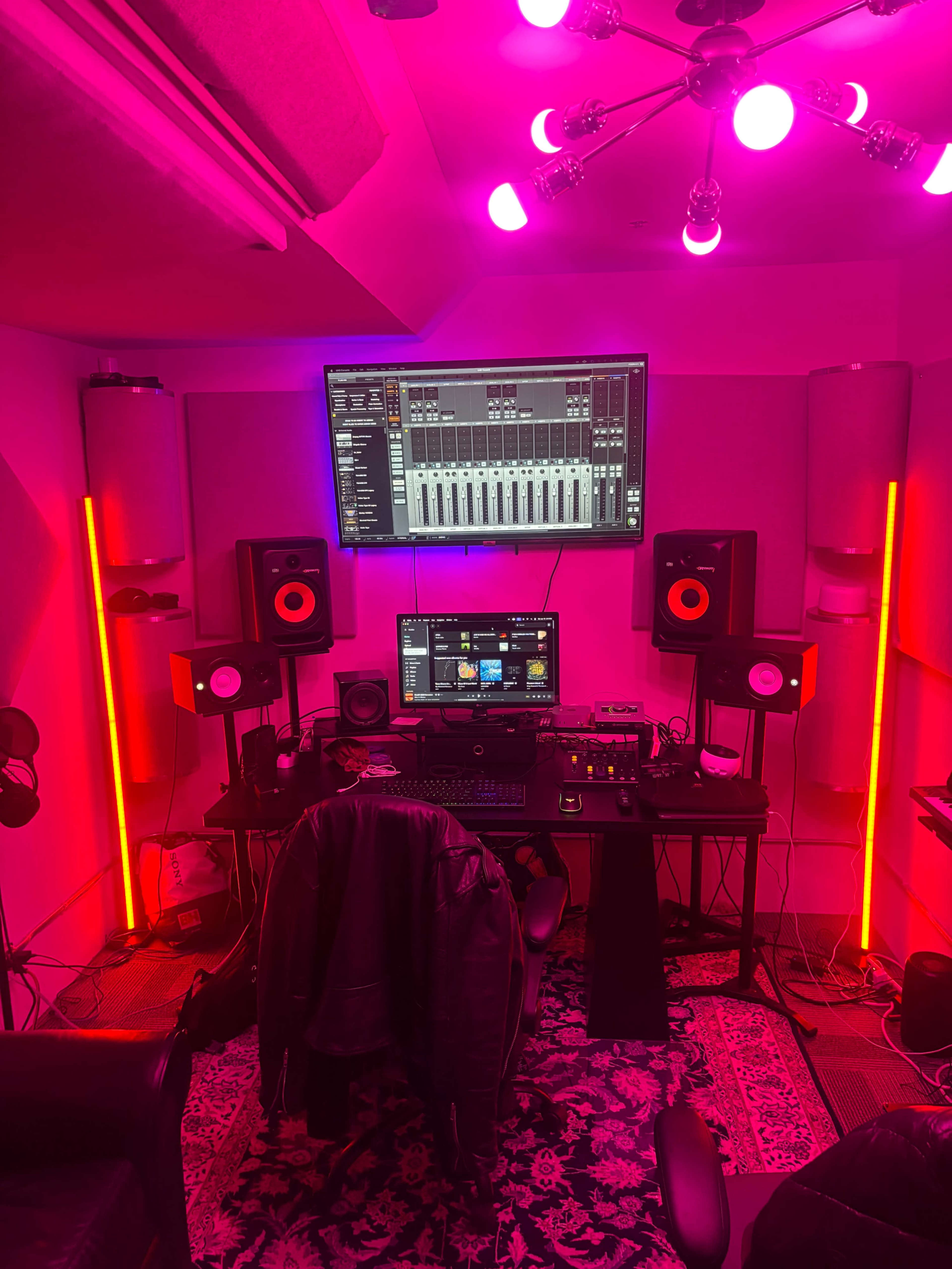 The image shows a music production studio with a desk equipped with audio monitors, a computer, and colorful lighting.