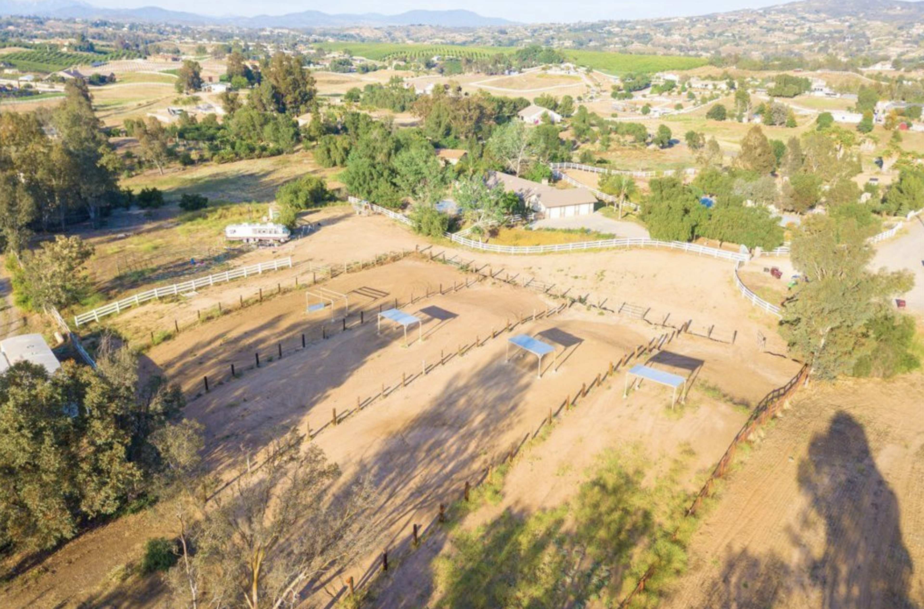 The image shows an aerial view of a rural area featuring fenced horse enclosures, houses, and agricultural fields.