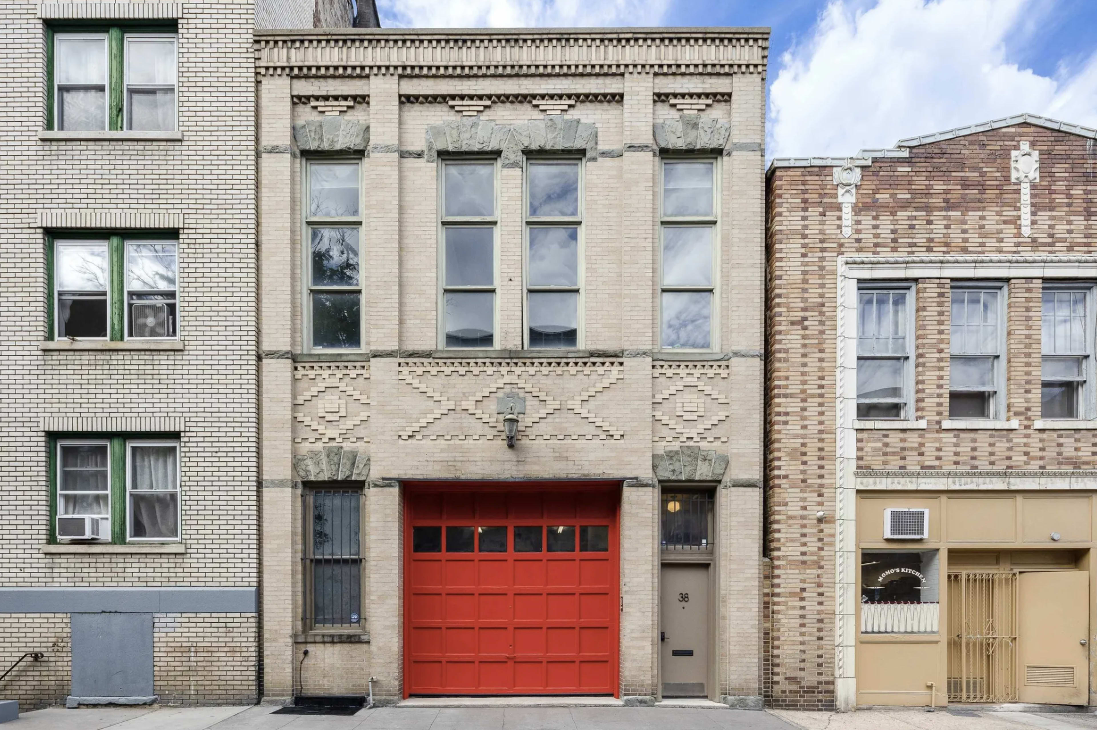 A three-story brick building with decorative features and a bright red garage door, flanked by two other brick structures.