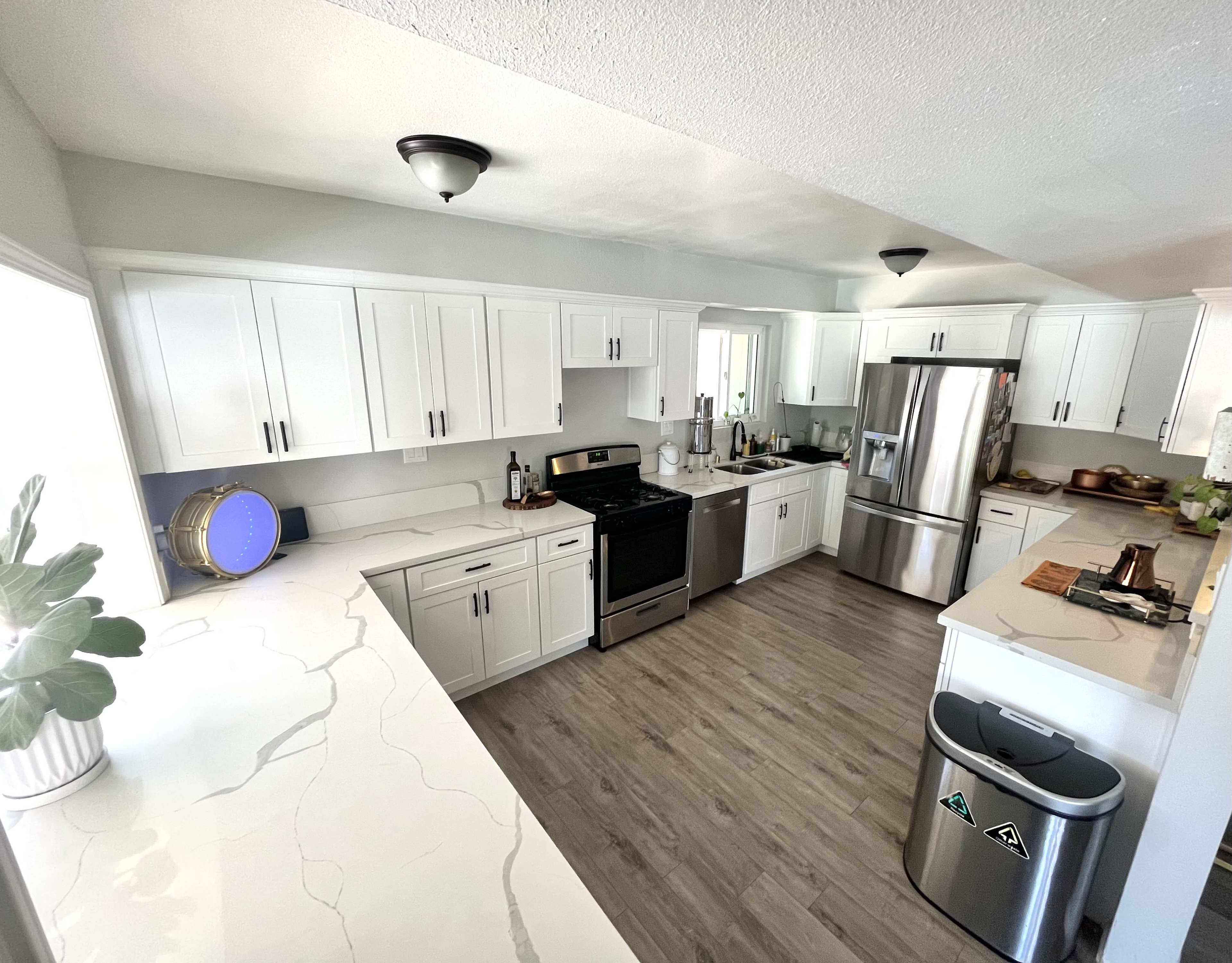 A modern kitchen with white cabinets, a stainless steel refrigerator, and a marble countertop.