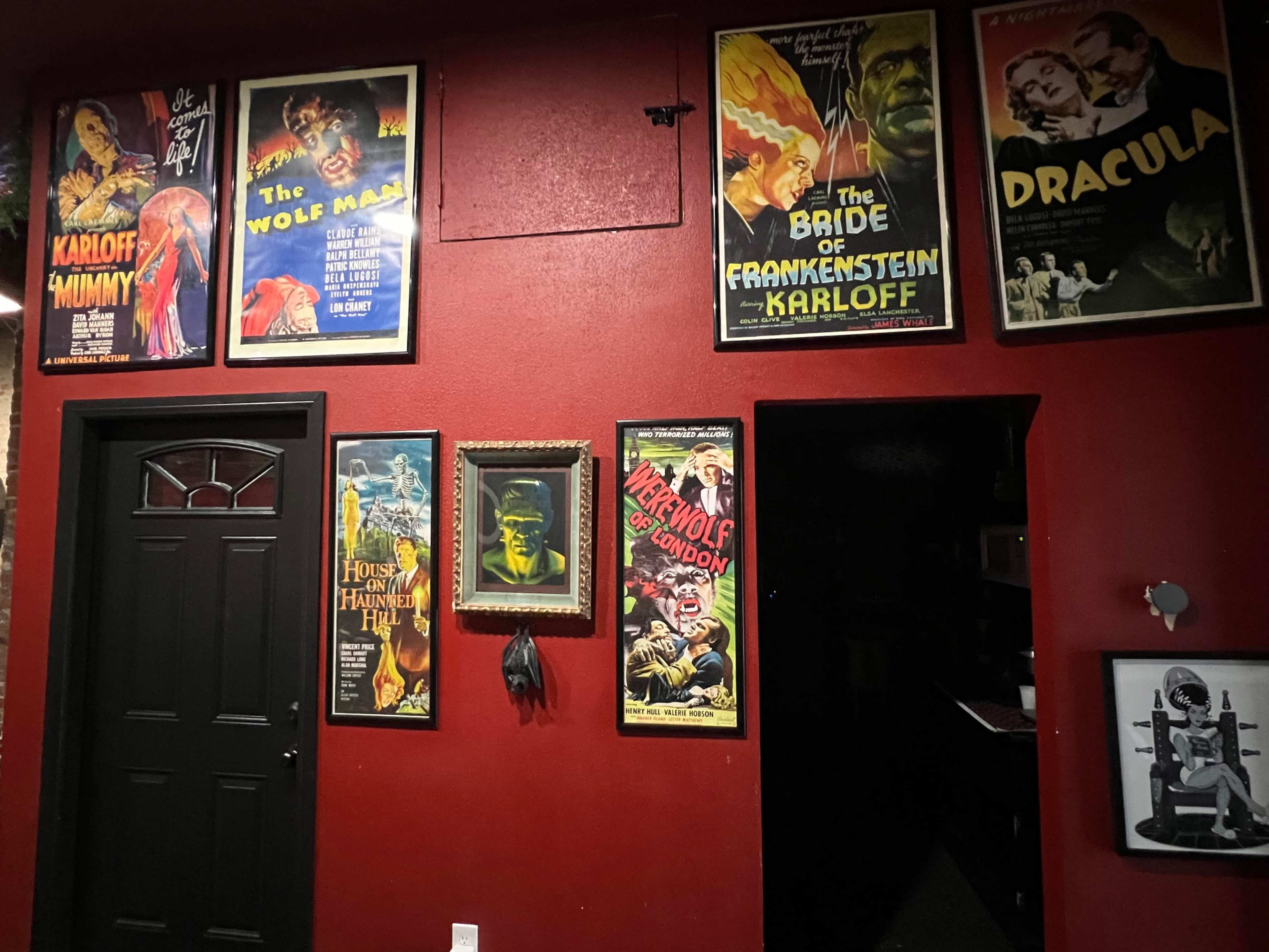 A red wall adorned with vintage horror movie posters featuring titles like "Dracula," "The Wolf Man," and "The Bride of Frankenstein."