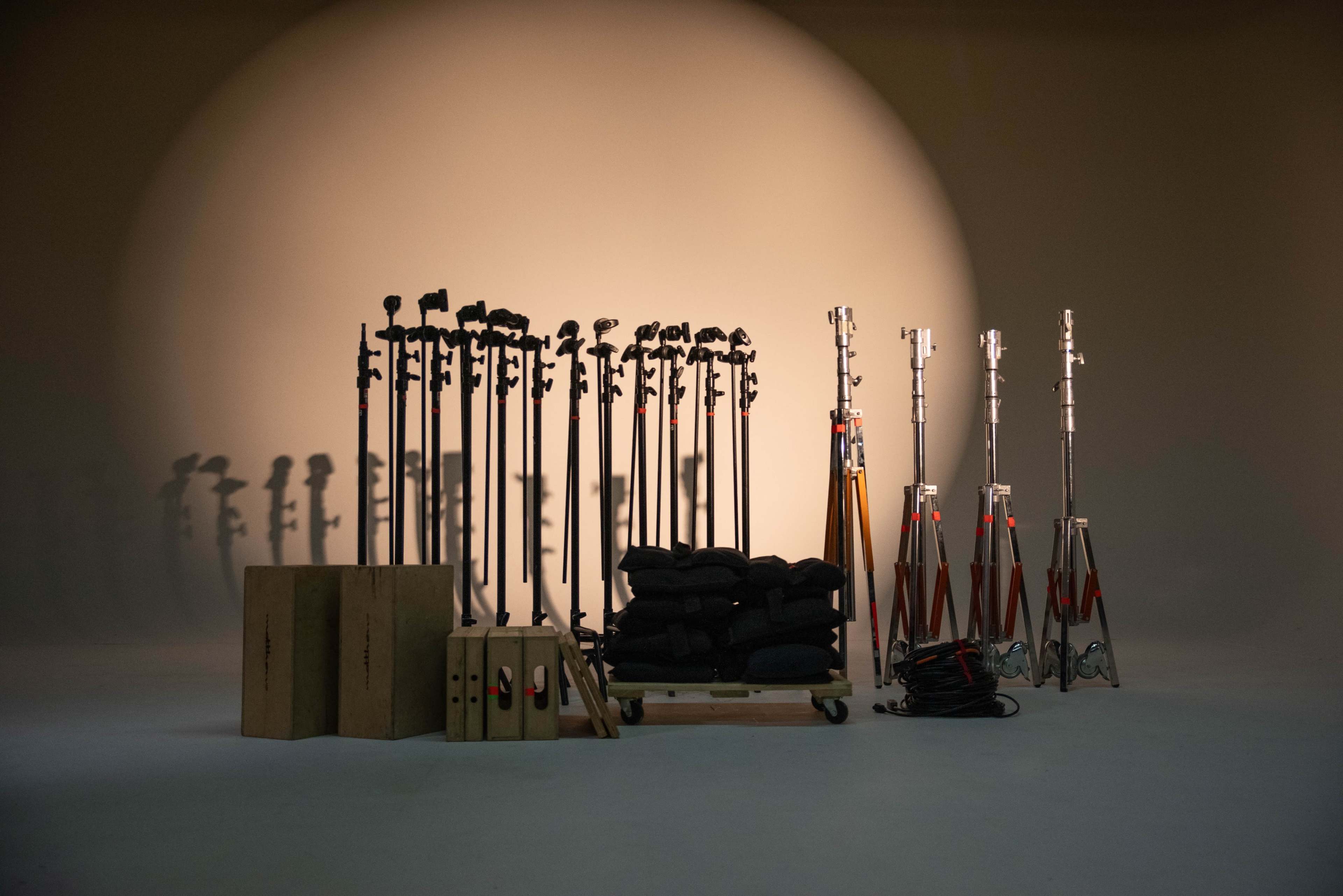 A collection of photography equipment, including light stands, weights, and wooden boxes, arranged in a studio with a circular light backdrop.