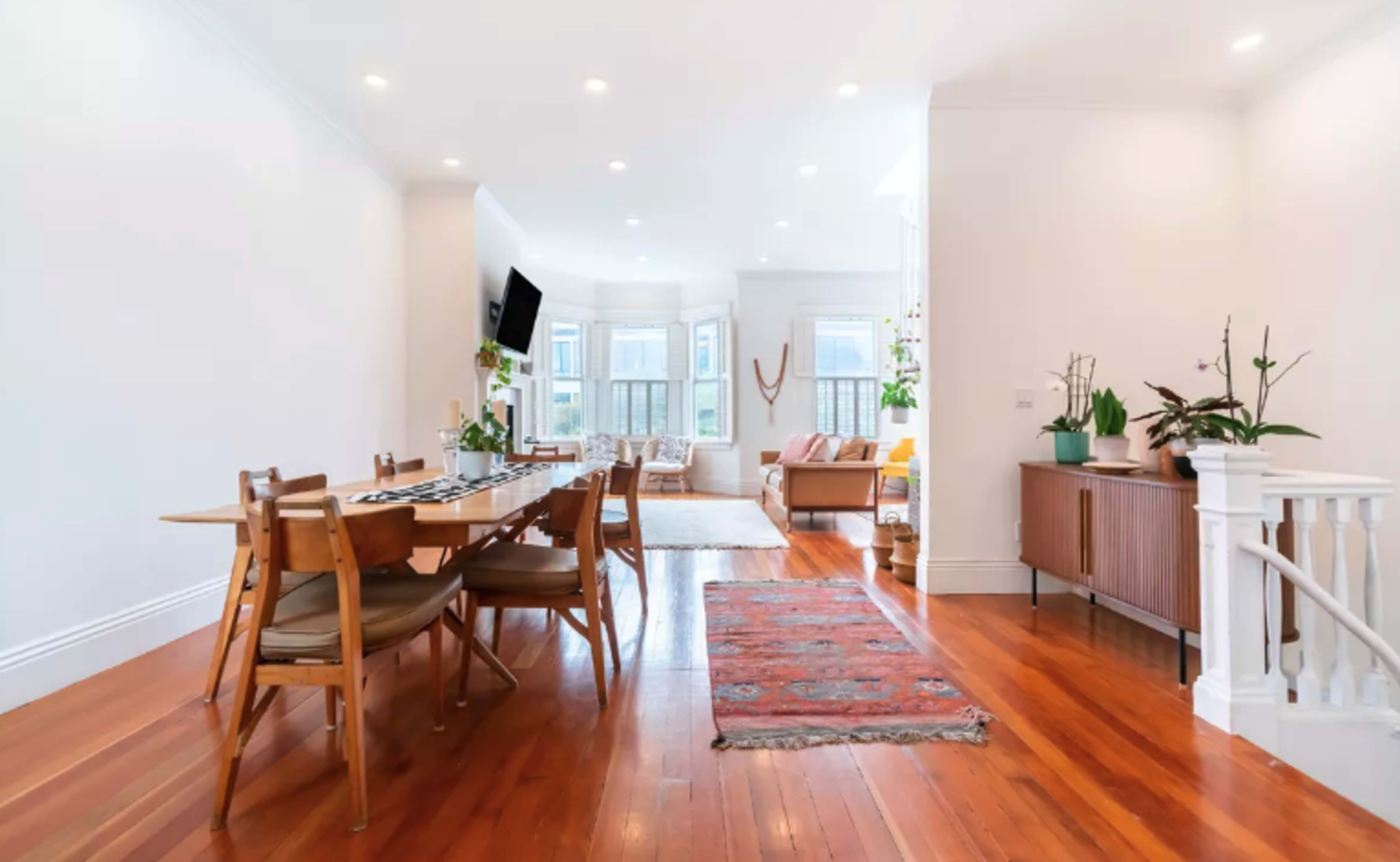 A modern, open-plan living and dining area with a long wooden table, surrounded by chairs, and a seating area in the background.