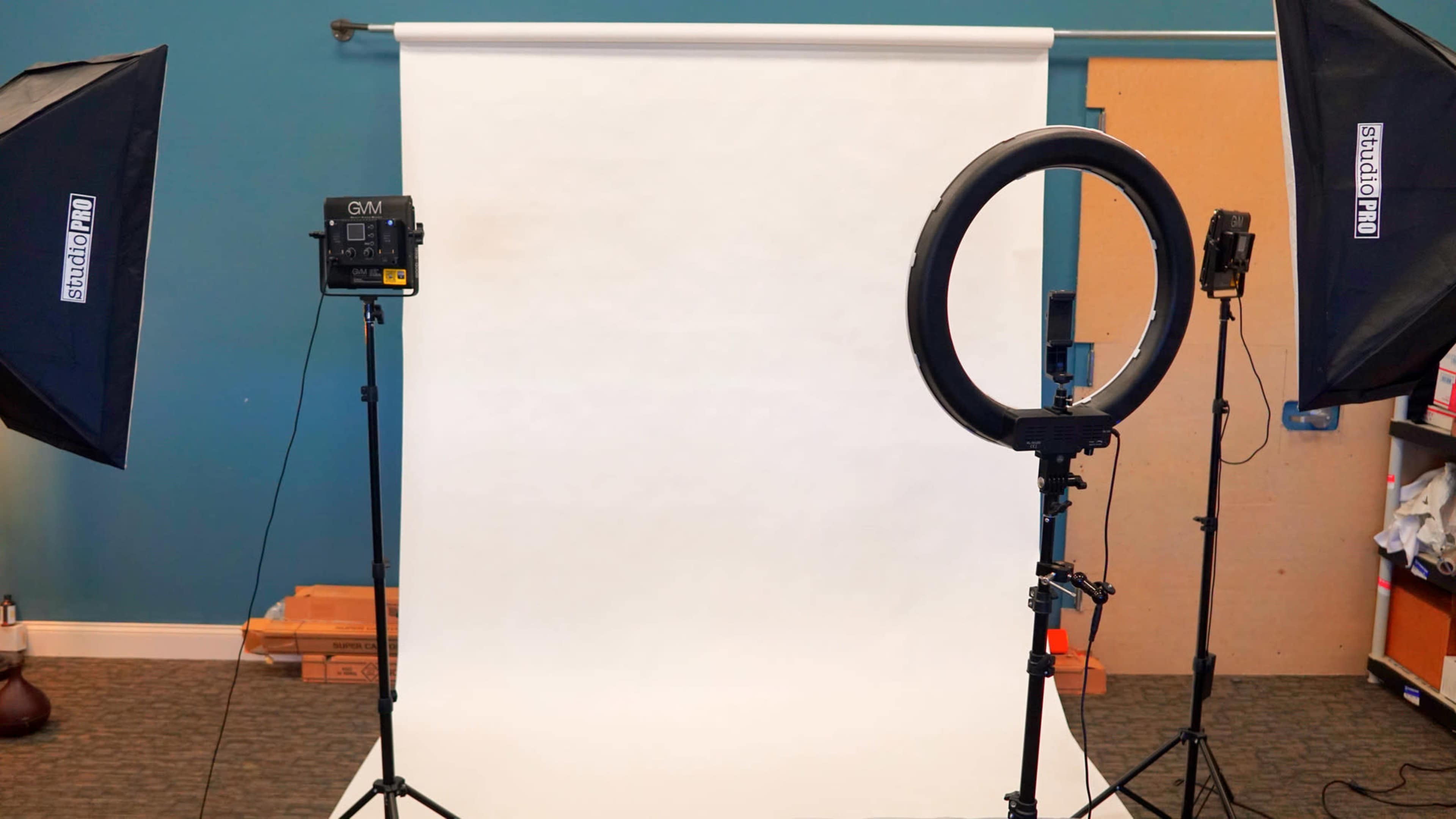 The image shows a photography setup with a white backdrop, a ring light, and two studio lights on tripods.