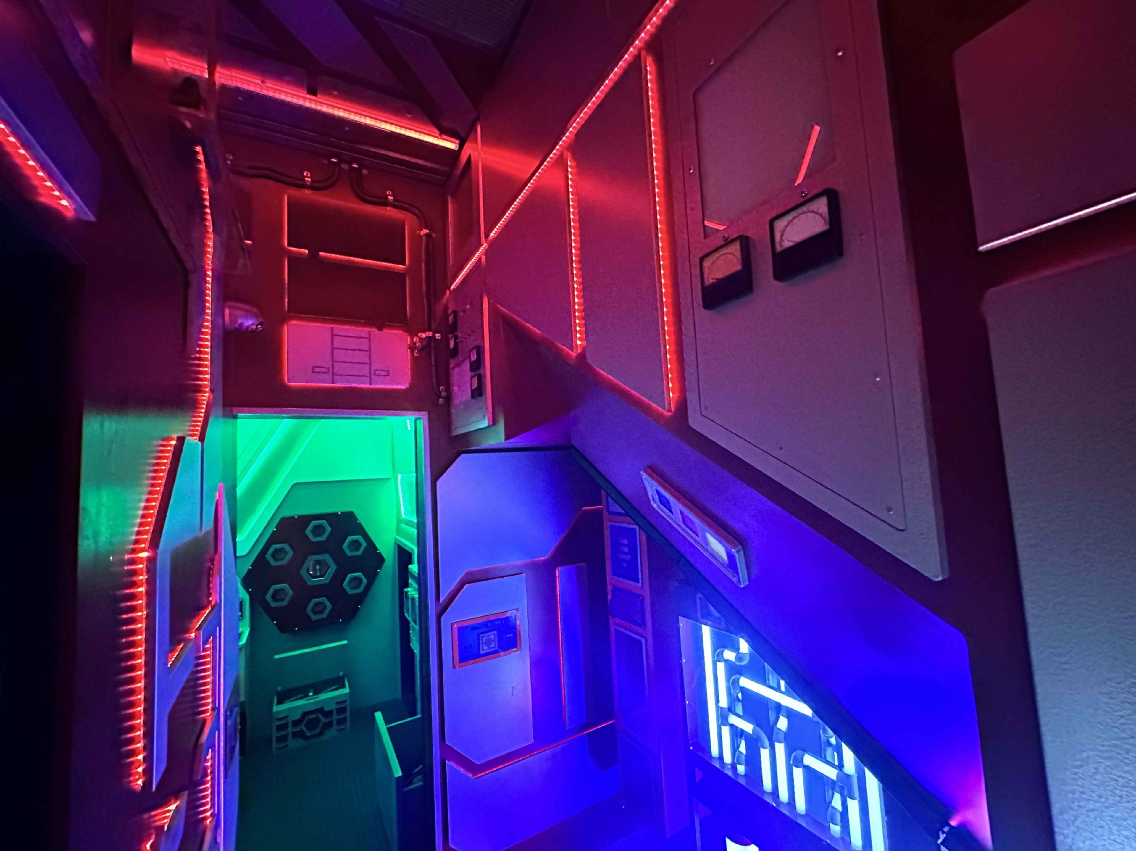 The interior of a spaceship-like environment features vibrant LED lighting and futuristic panels along a staircase leading to additional rooms.