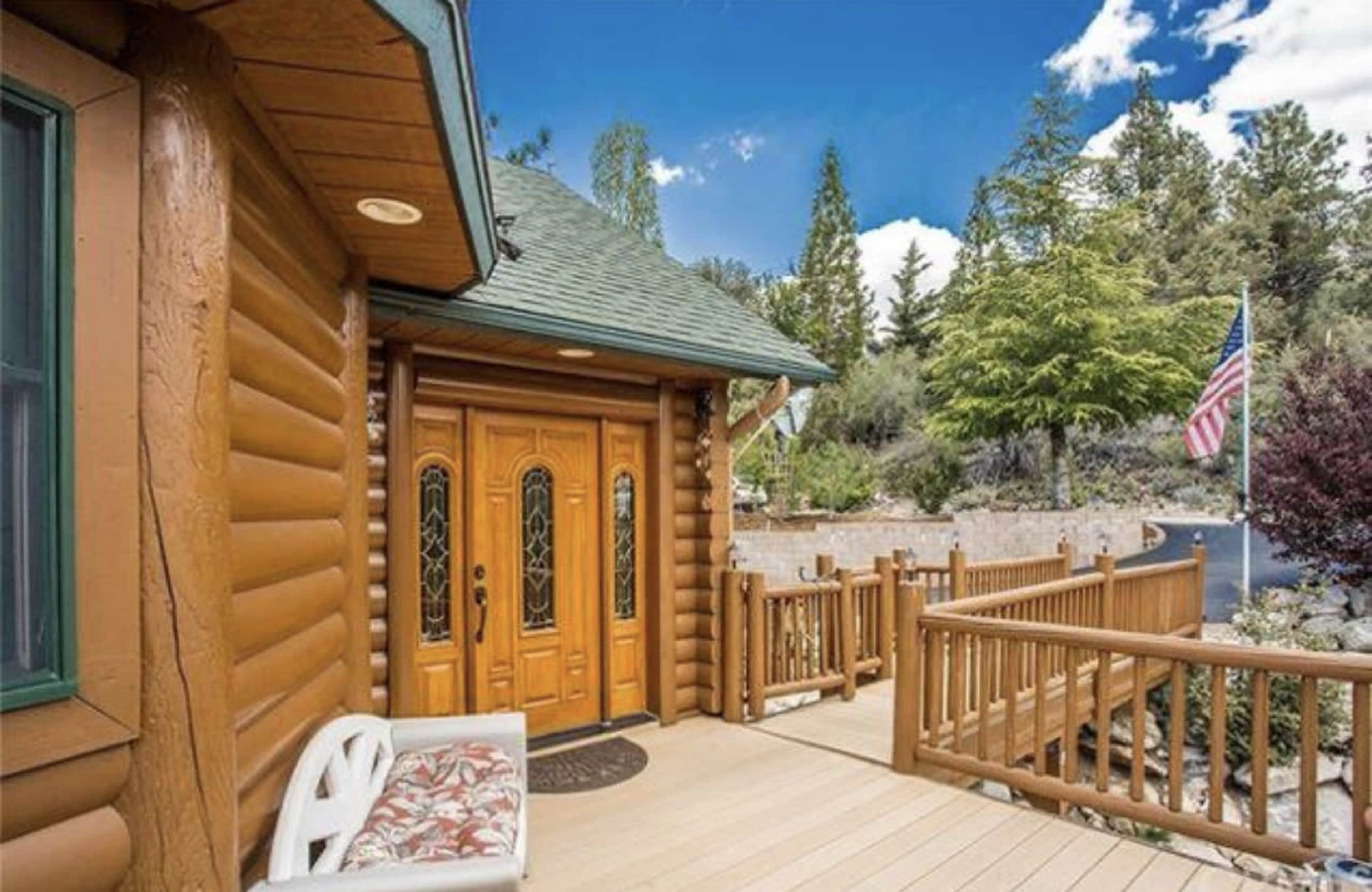 A log cabin entrance with wooden doors, a porch, and an American flag nearby.