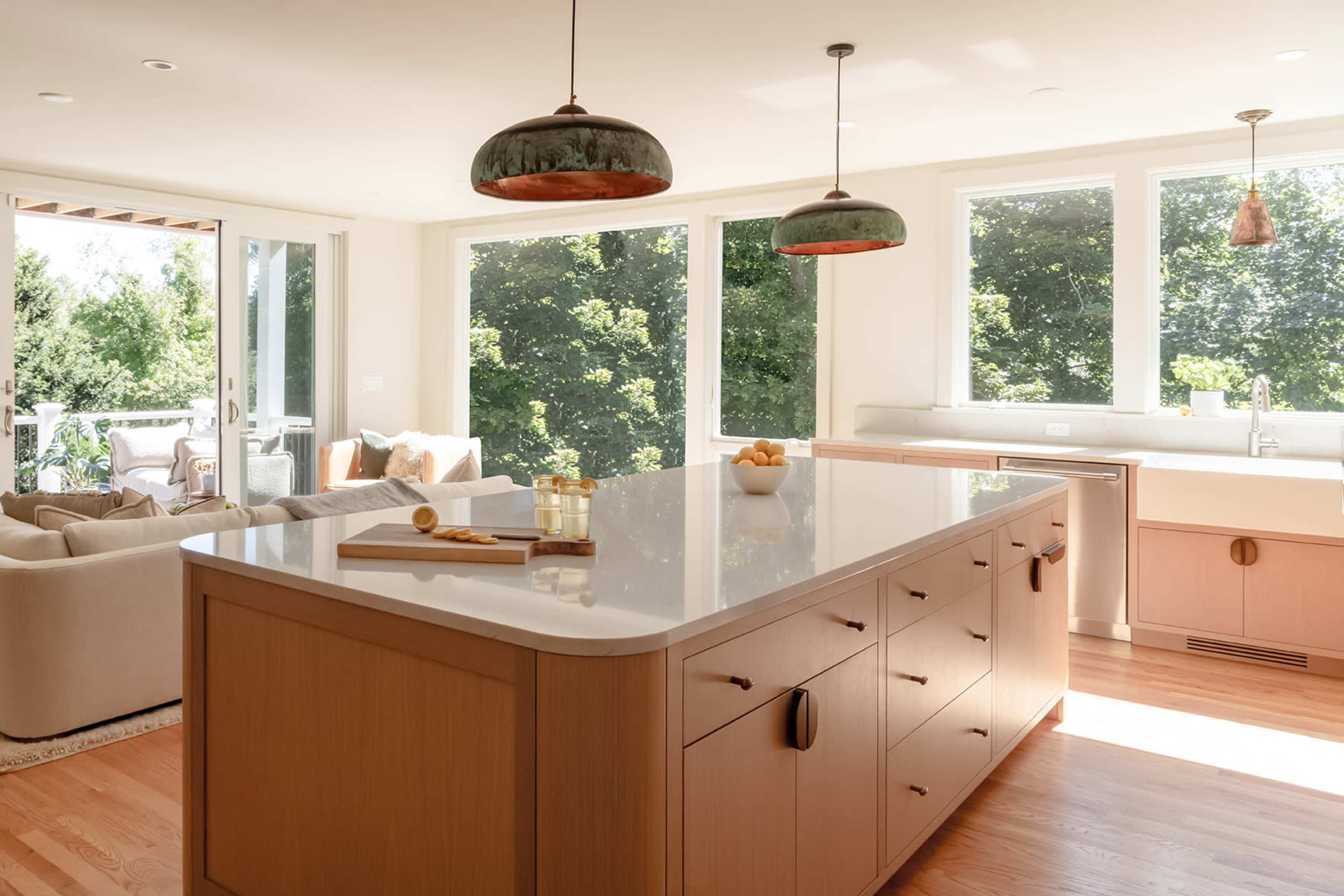 The image shows a modern kitchen with a large central island, quartz countertops, and multiple windows allowing natural light to flood the space.