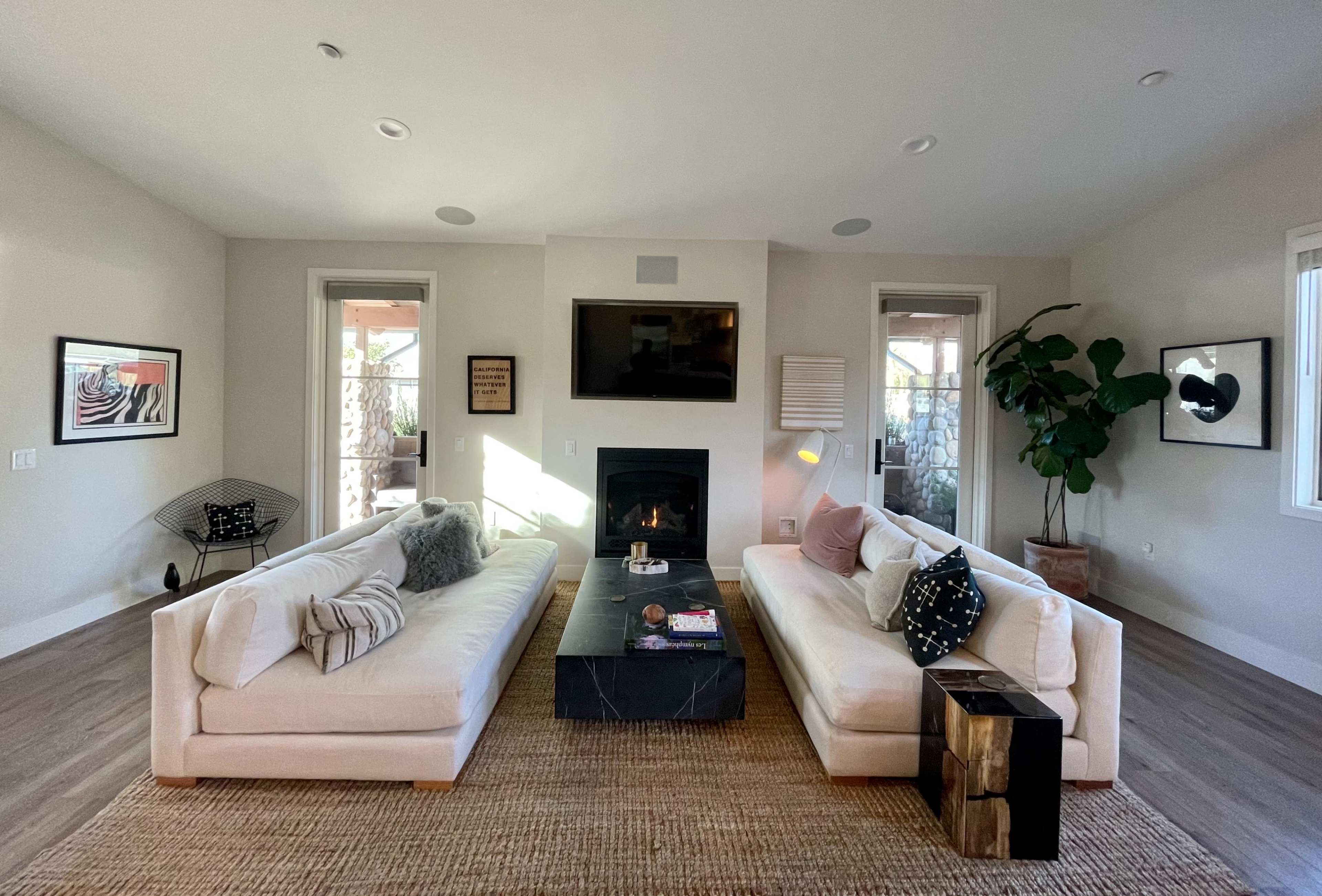 The living room features two white sofas facing each other, a black coffee table in the center, and a fireplace against a light-colored wall.