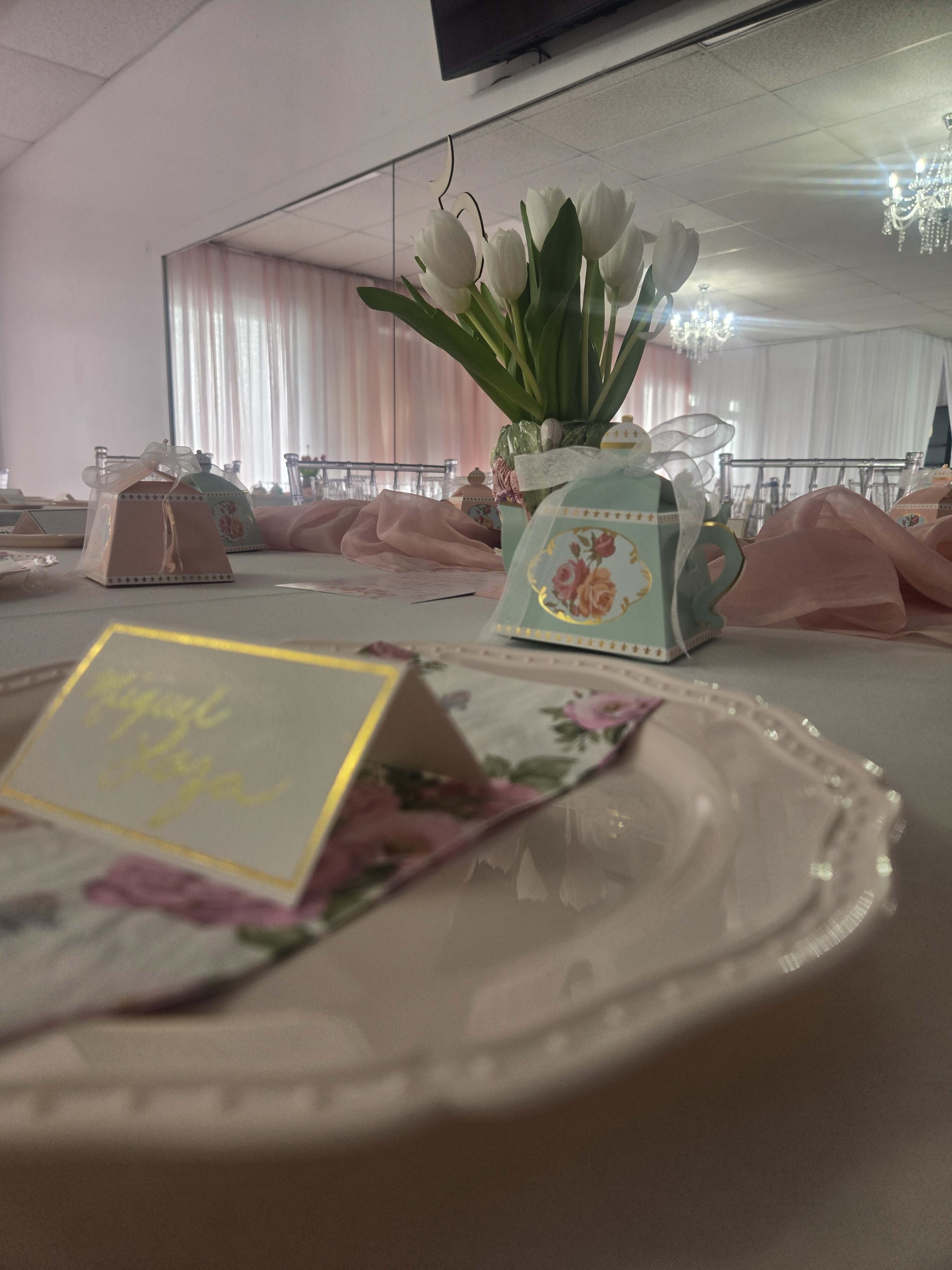 A table is elegantly set with floral-themed place cards, decorative boxes, and a vase of white tulips.