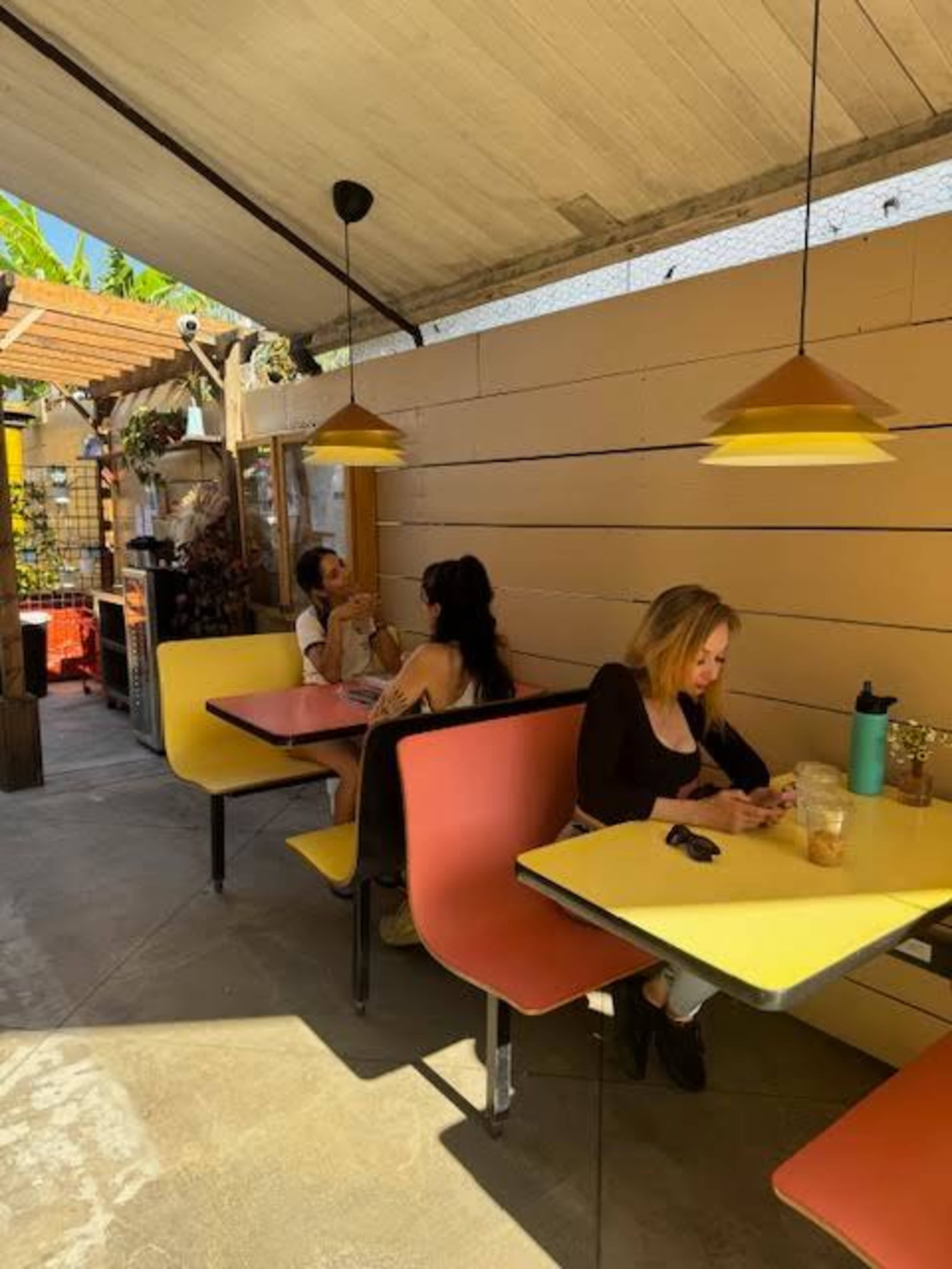 The image shows a small outdoor cafe with patrons seated at colorful tables under a covered area.