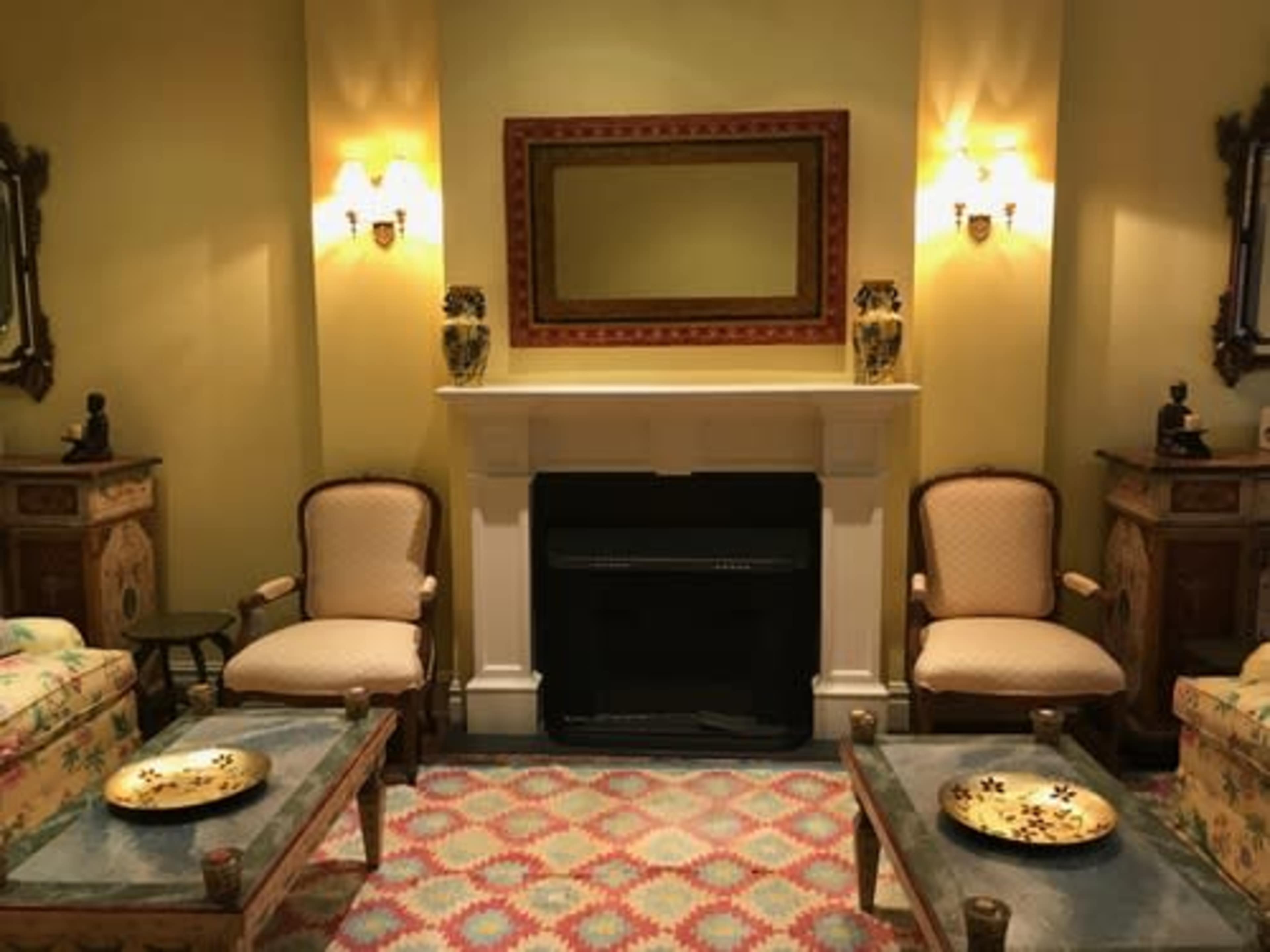 A cozy living room with two upholstered chairs, a fireplace, a large mirror, and decorative accents on the walls.