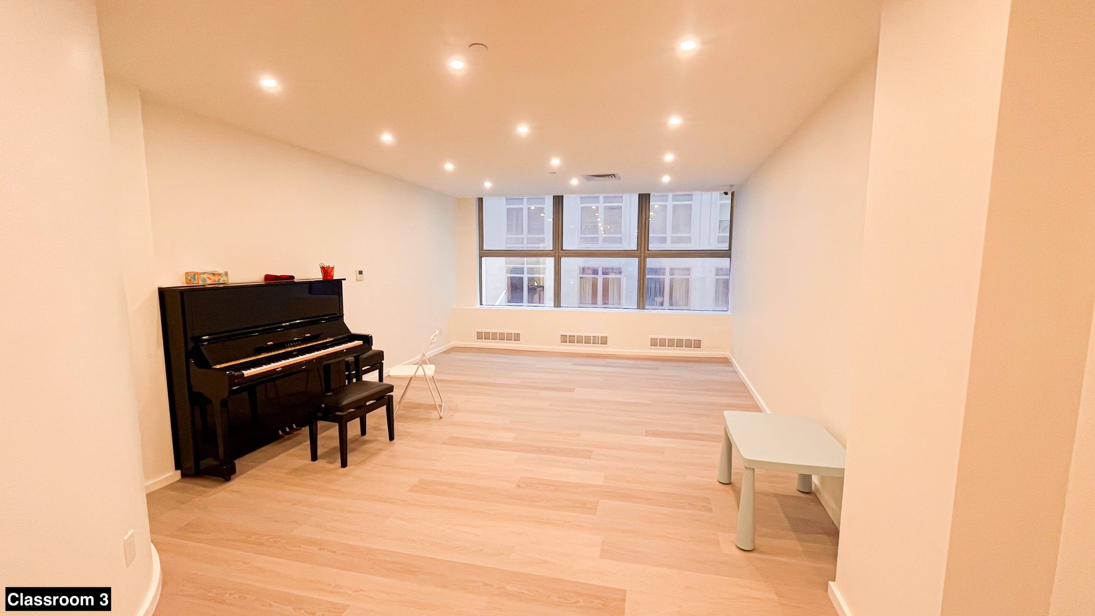 The image shows a spacious, well-lit room with a black piano and a small table and chair.