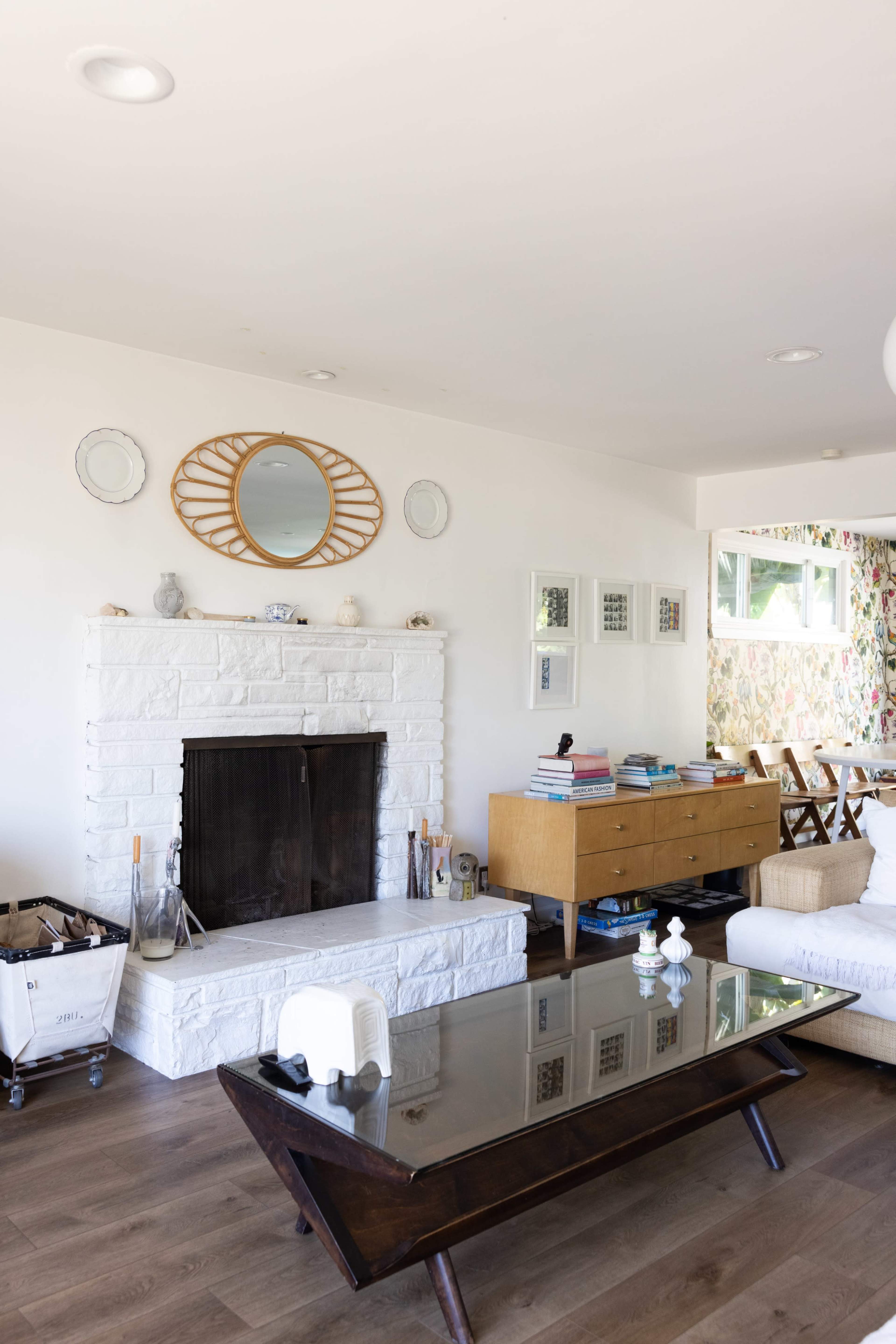 A living room with a white stone fireplace, a wooden coffee table, and a decorative mirror above the mantelpiece.