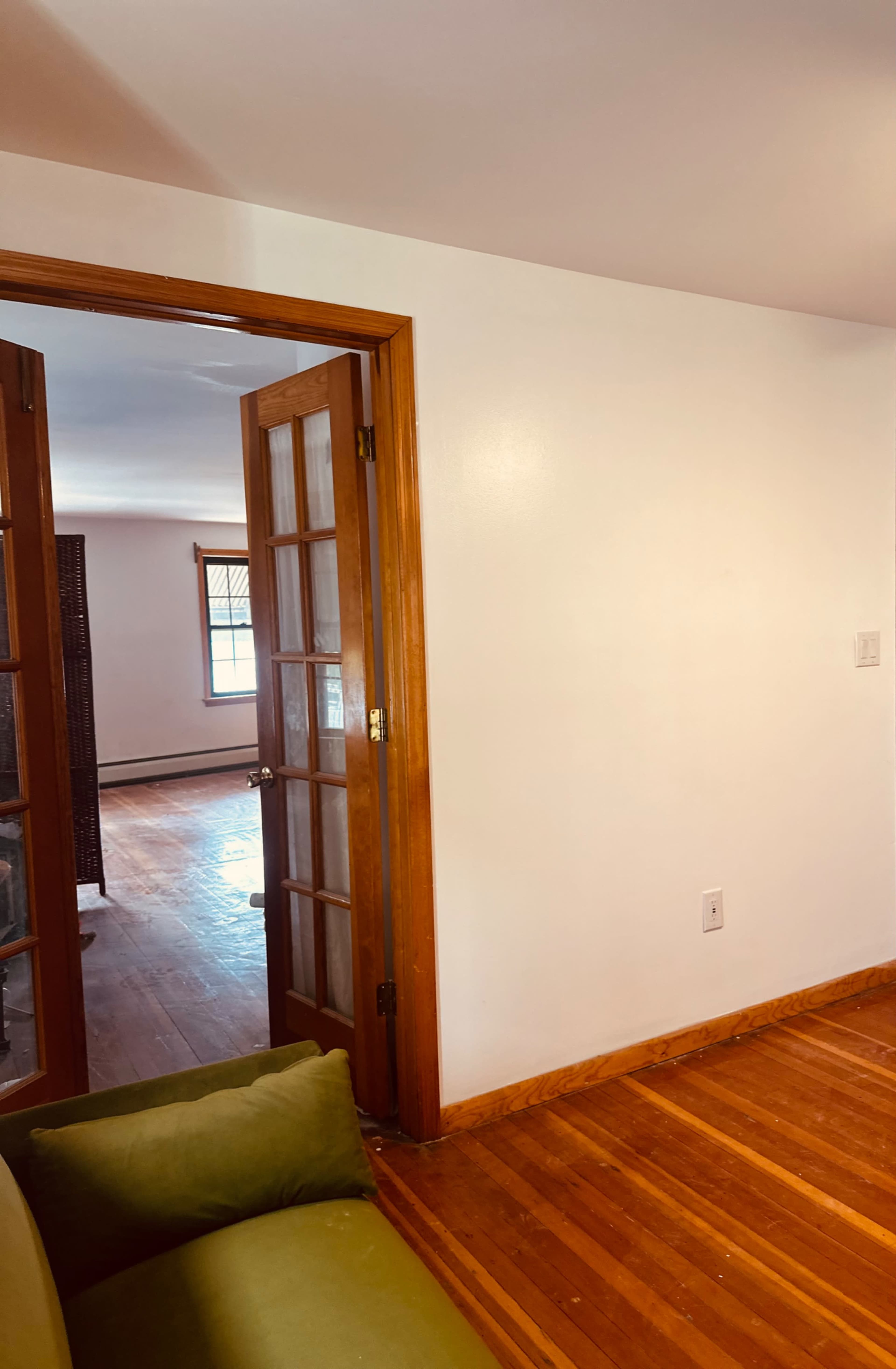 A doorway with wooden frame and glass panels leads to a room with hardwood floors and windows in the background.