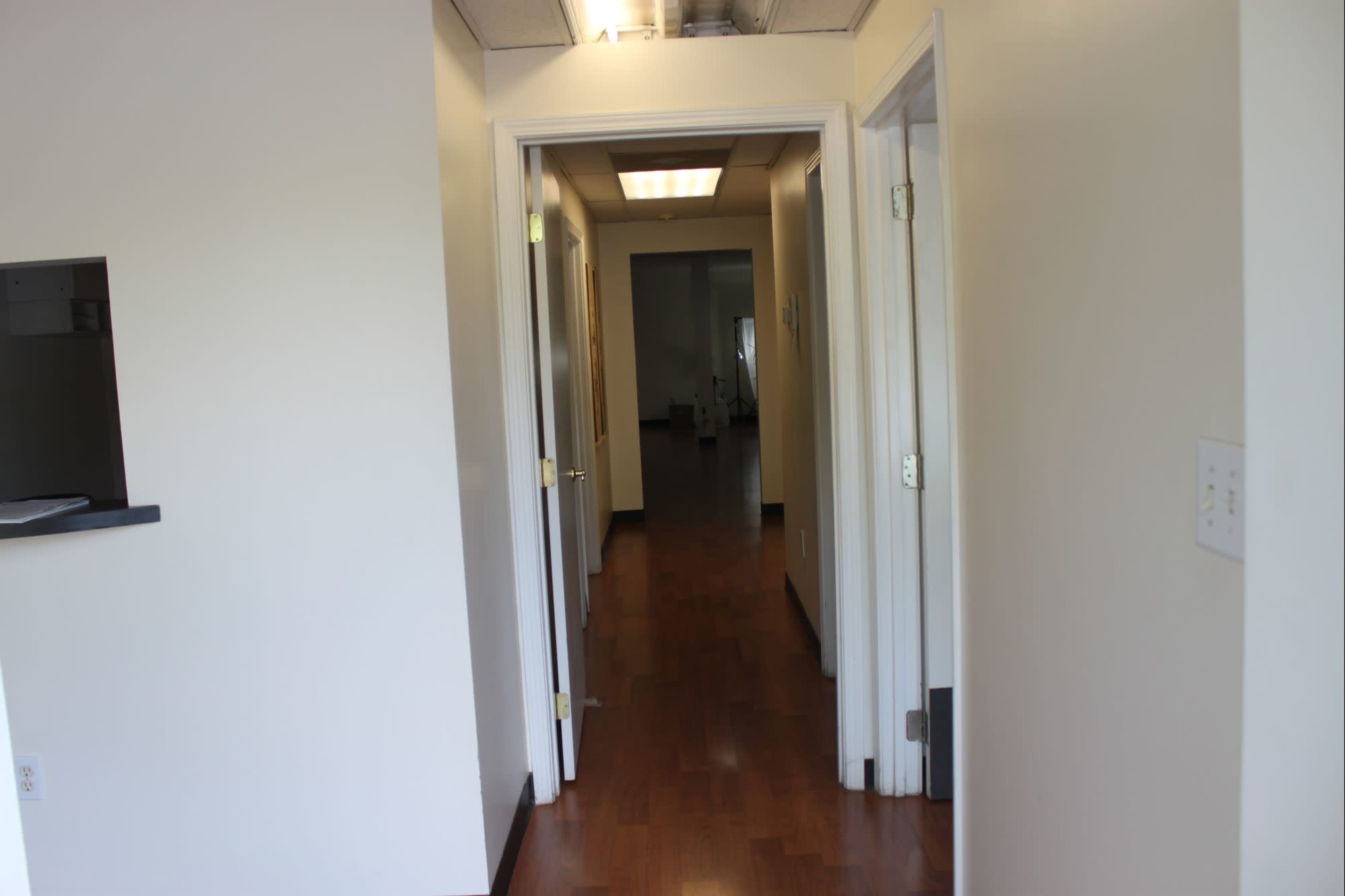 The image shows a hallway with doors on either side leading to different rooms, featuring wooden flooring and neutral-colored walls.