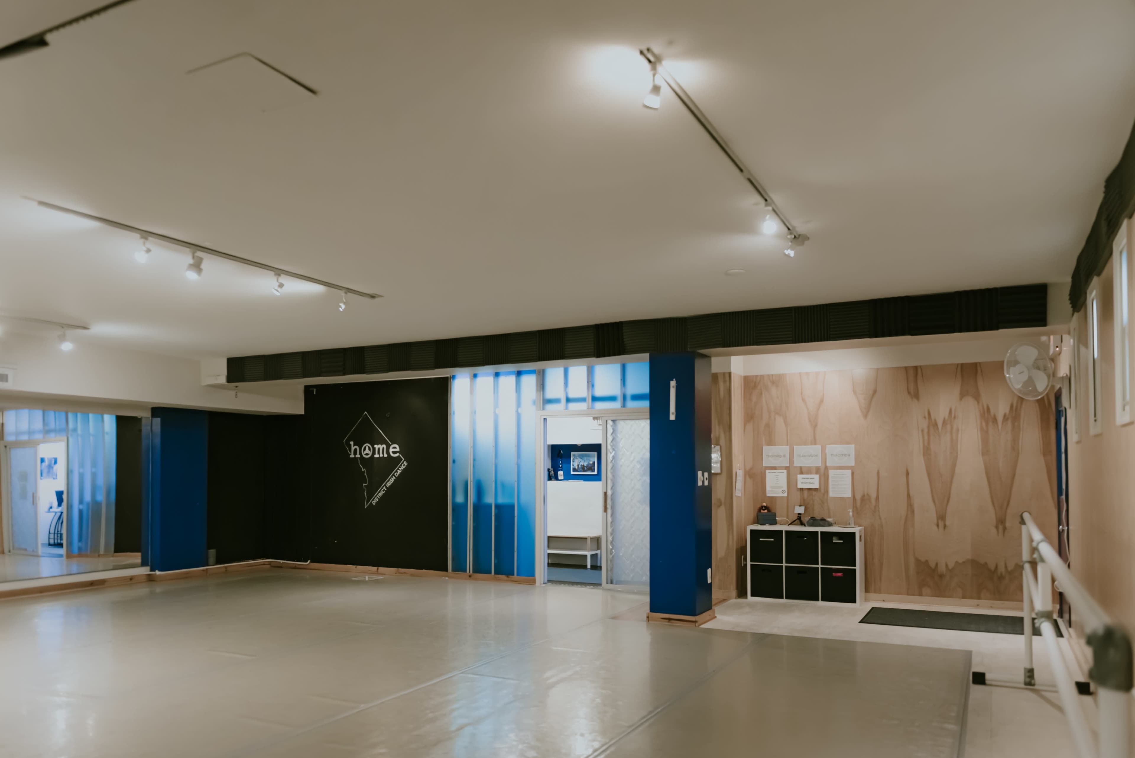 A spacious dance studio with wooden floors, mirrored walls, and a home-themed black wall on one side.