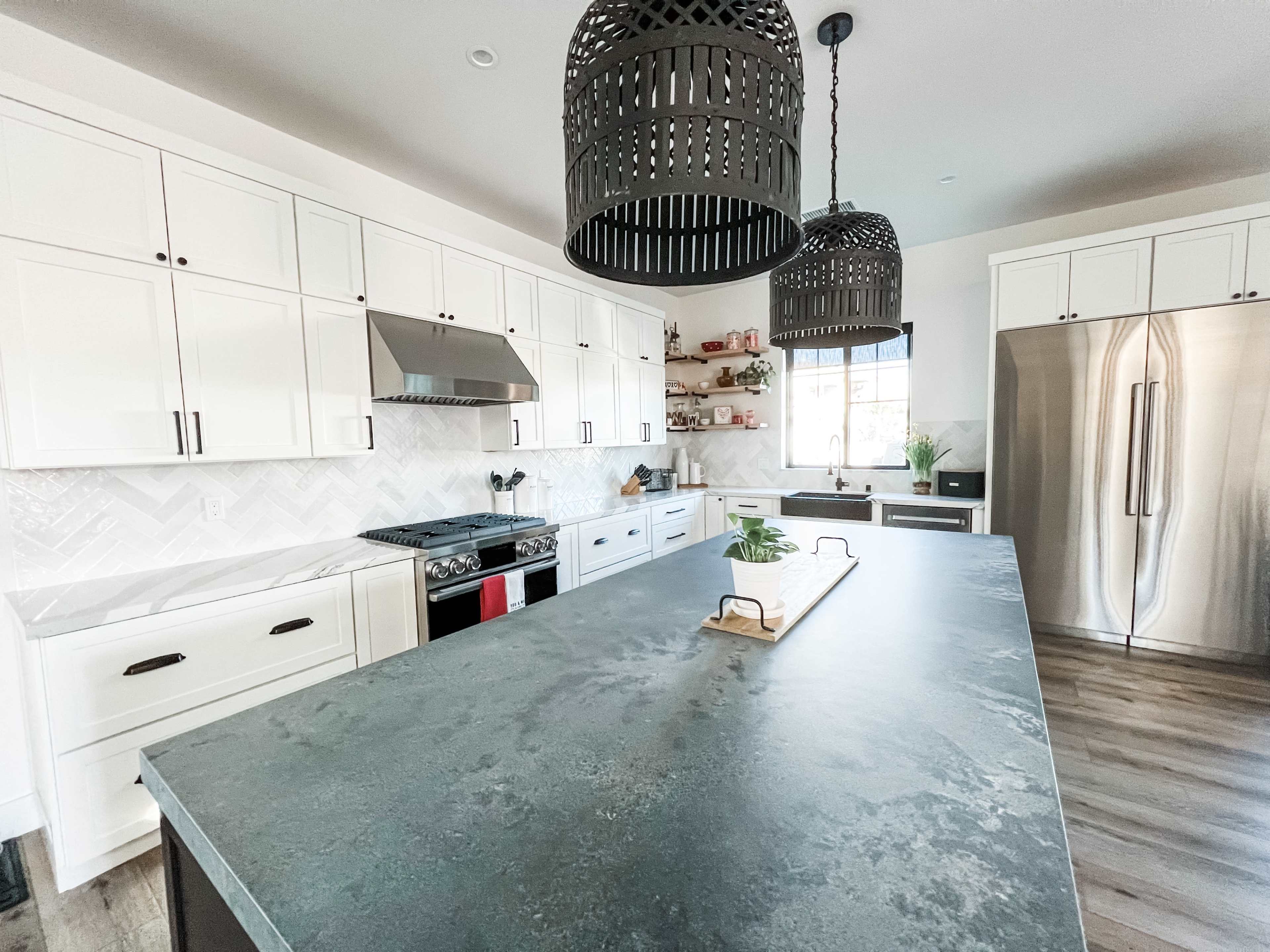 A modern kitchen features a large island with a dark countertop, white cabinetry, and two pendant lights hanging above.