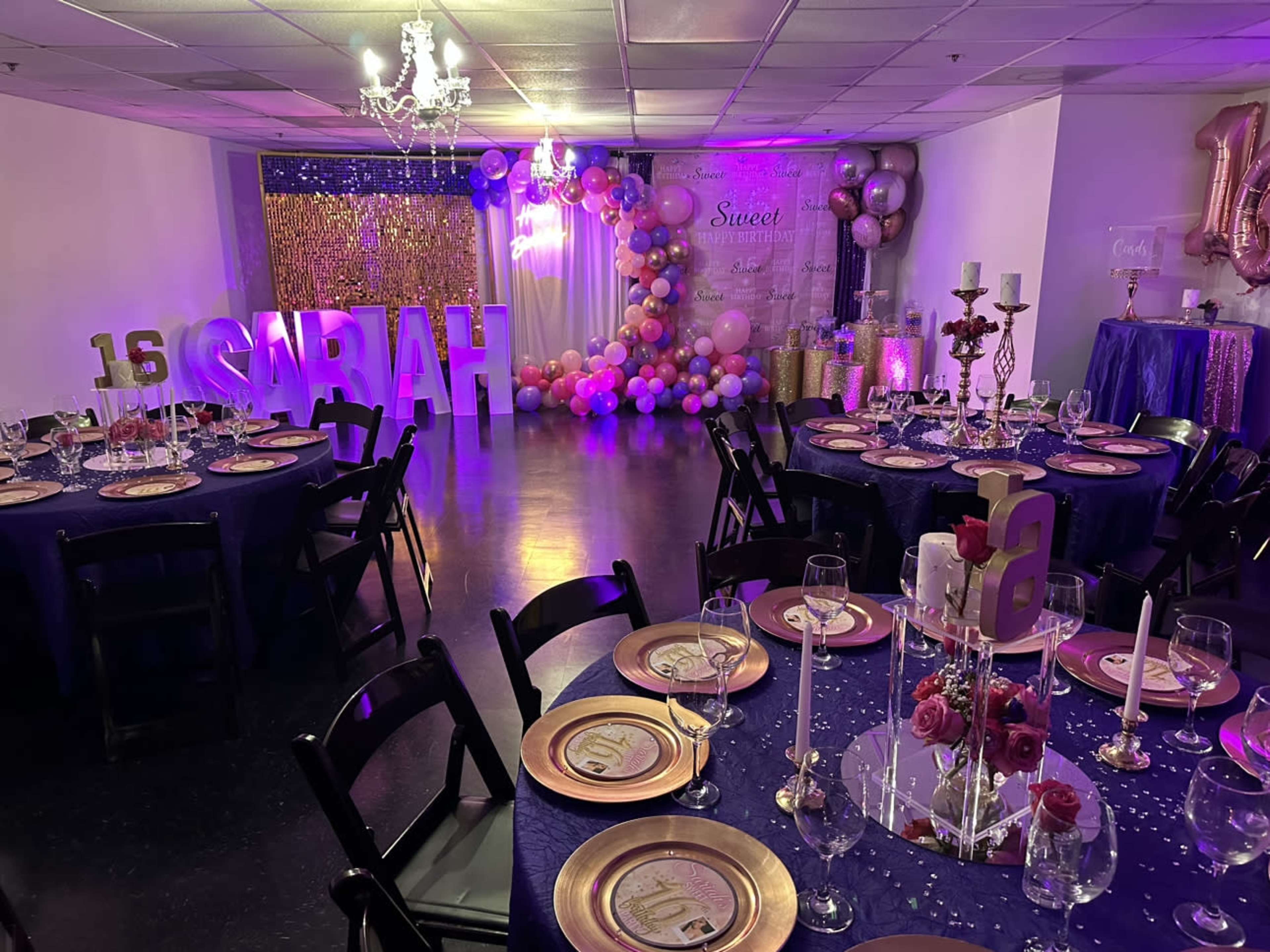 The image shows a decorated event space for a birthday celebration, featuring tables set with plates and glasses, a large "16" display, and colorful balloon arrangements.