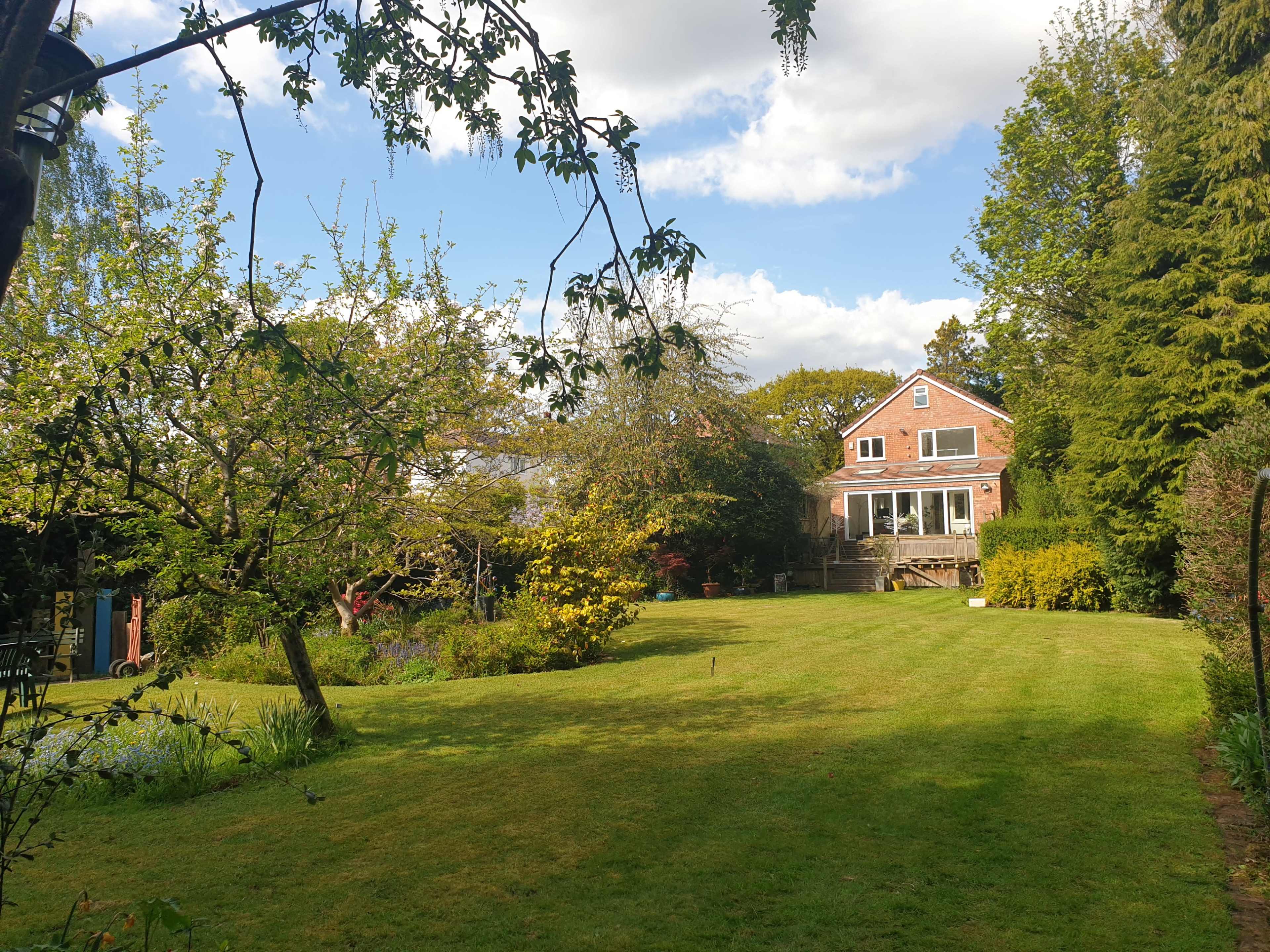 A well-maintained garden features a house with a deck, surrounded by trees and a neatly trimmed lawn.