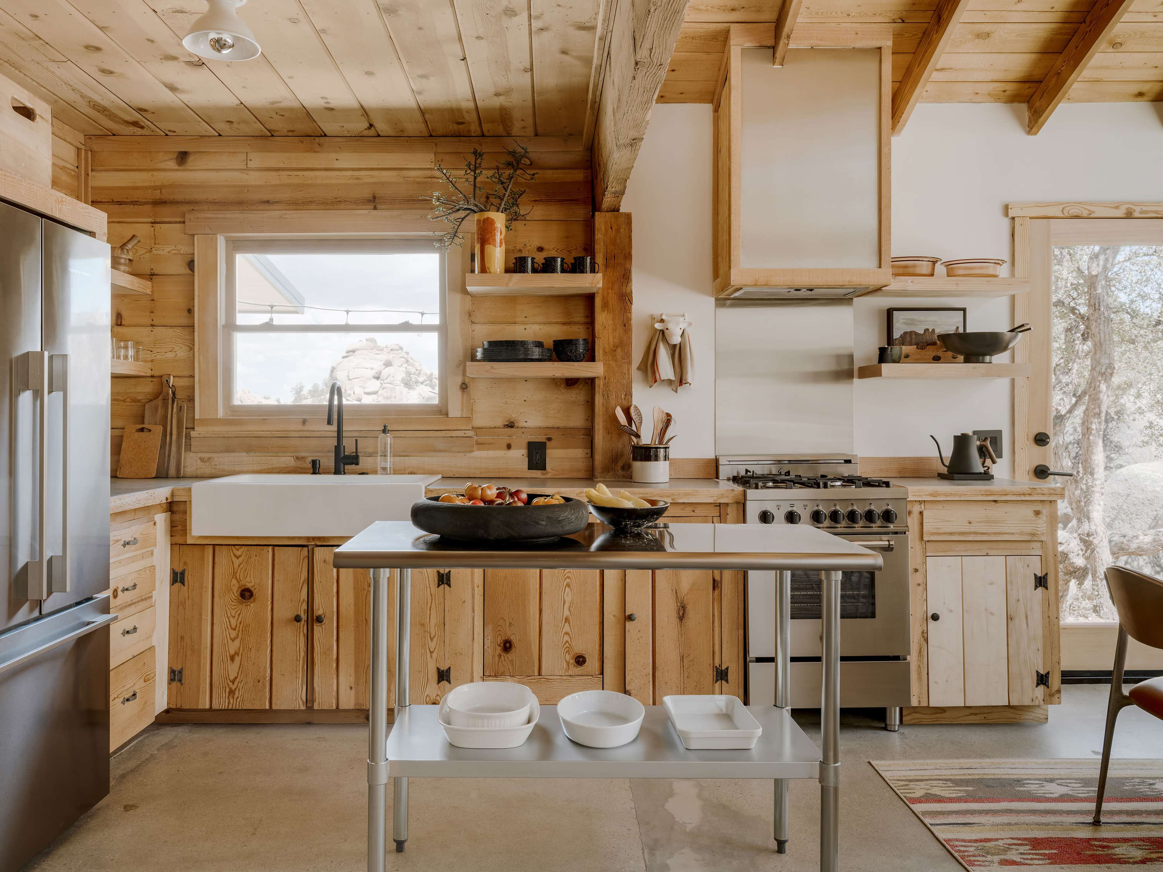 The kitchen features wooden cabinetry, a stainless steel refrigerator, and an island with white dishware on a concrete floor.
