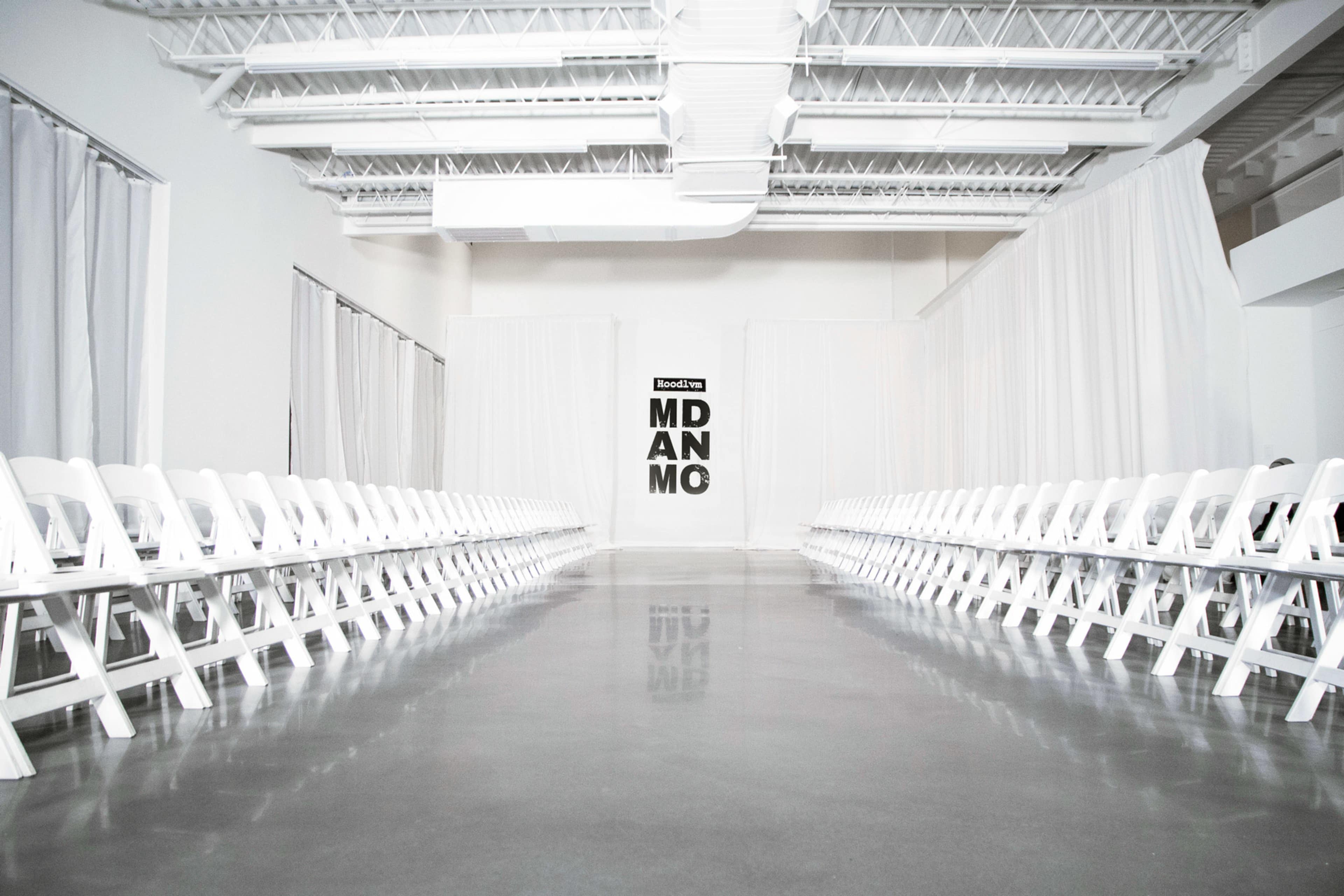 A vacant runway is flanked by rows of white chairs, with a large sign reading "MDANMO" at the far end.