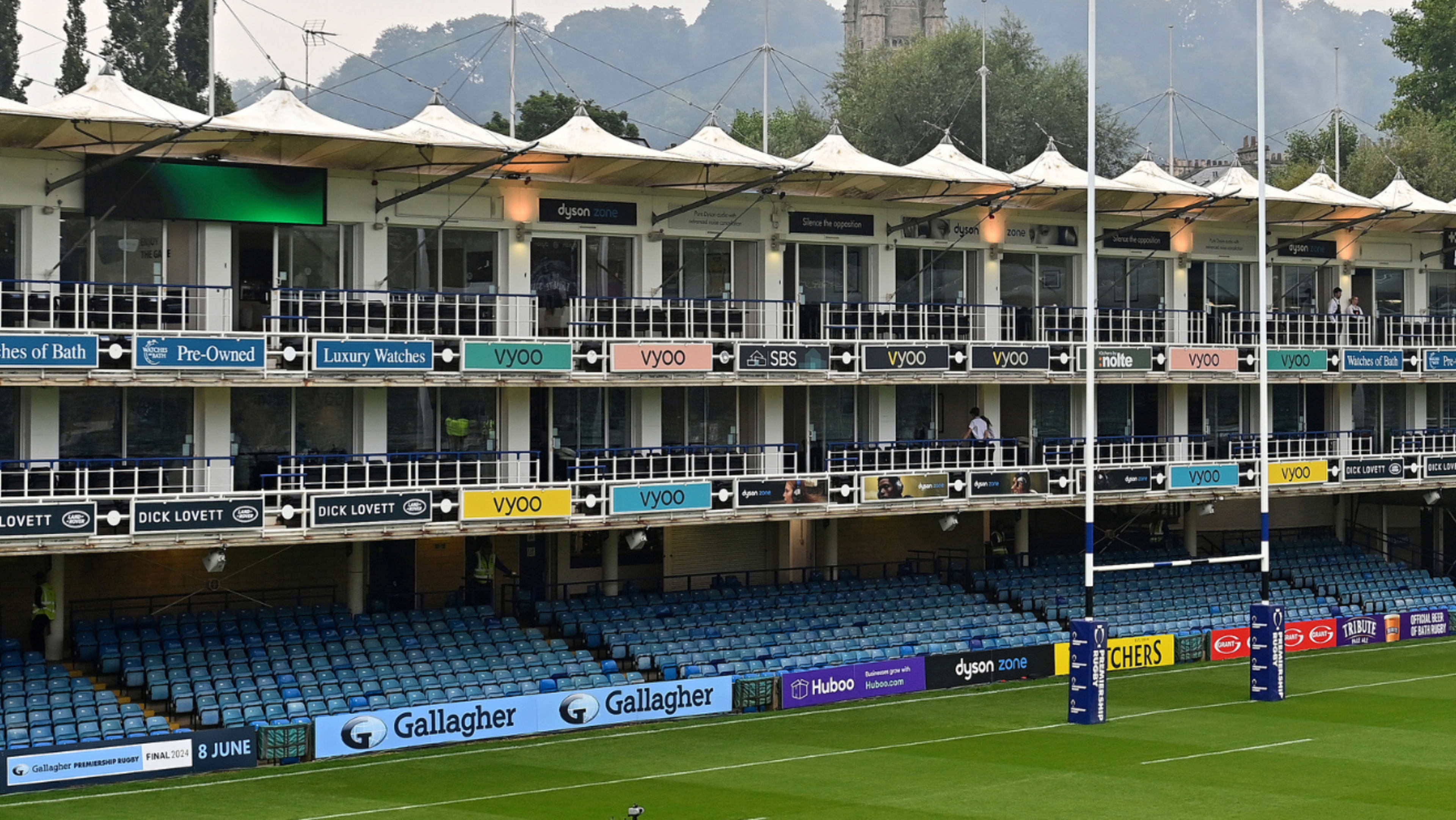 A row of luxury corporate boxes and seating overlooks a rugby field at a stadium.