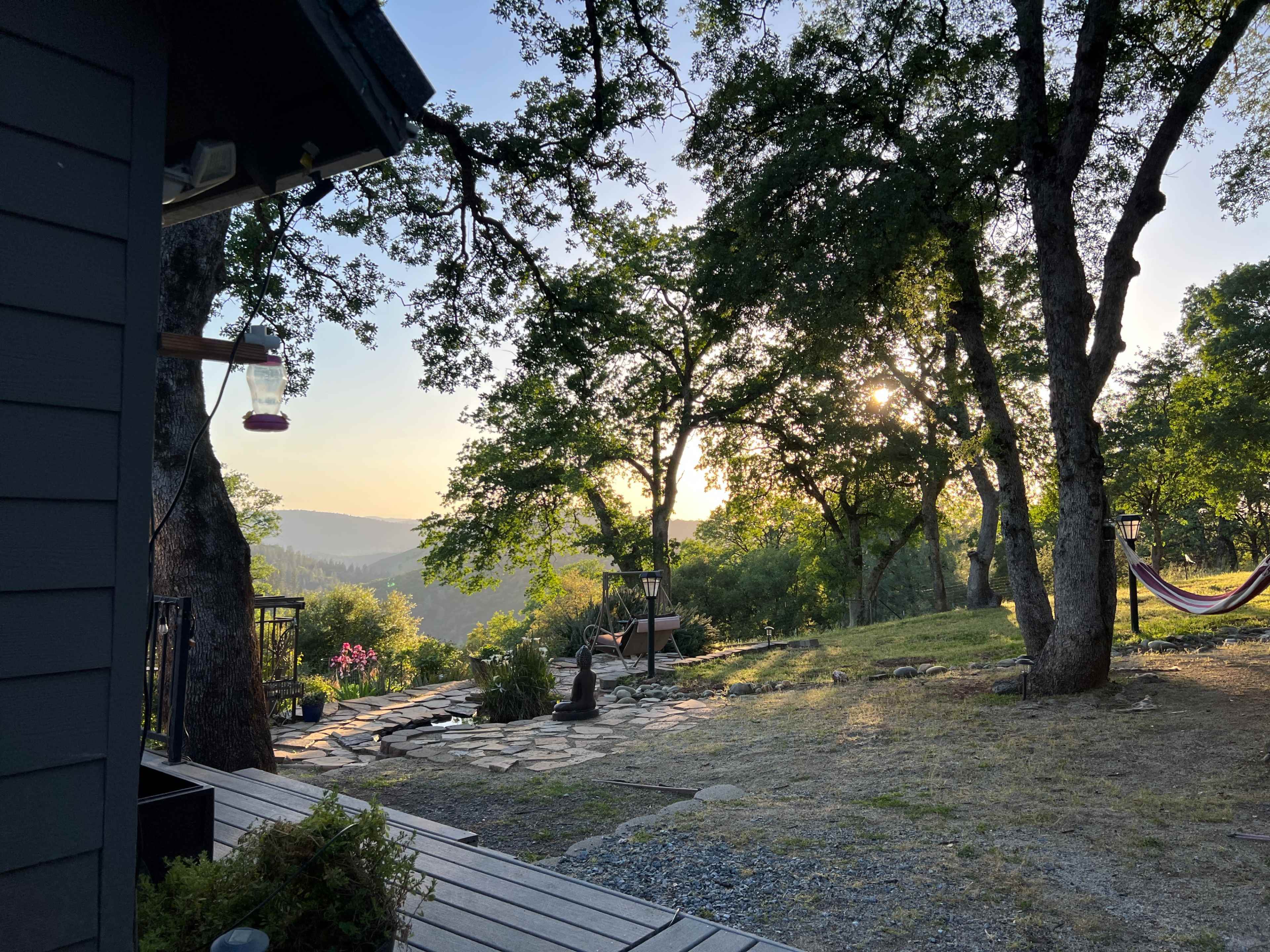 A serene outdoor setting with trees and a hammock, overlooking a distant valley at sunrise.