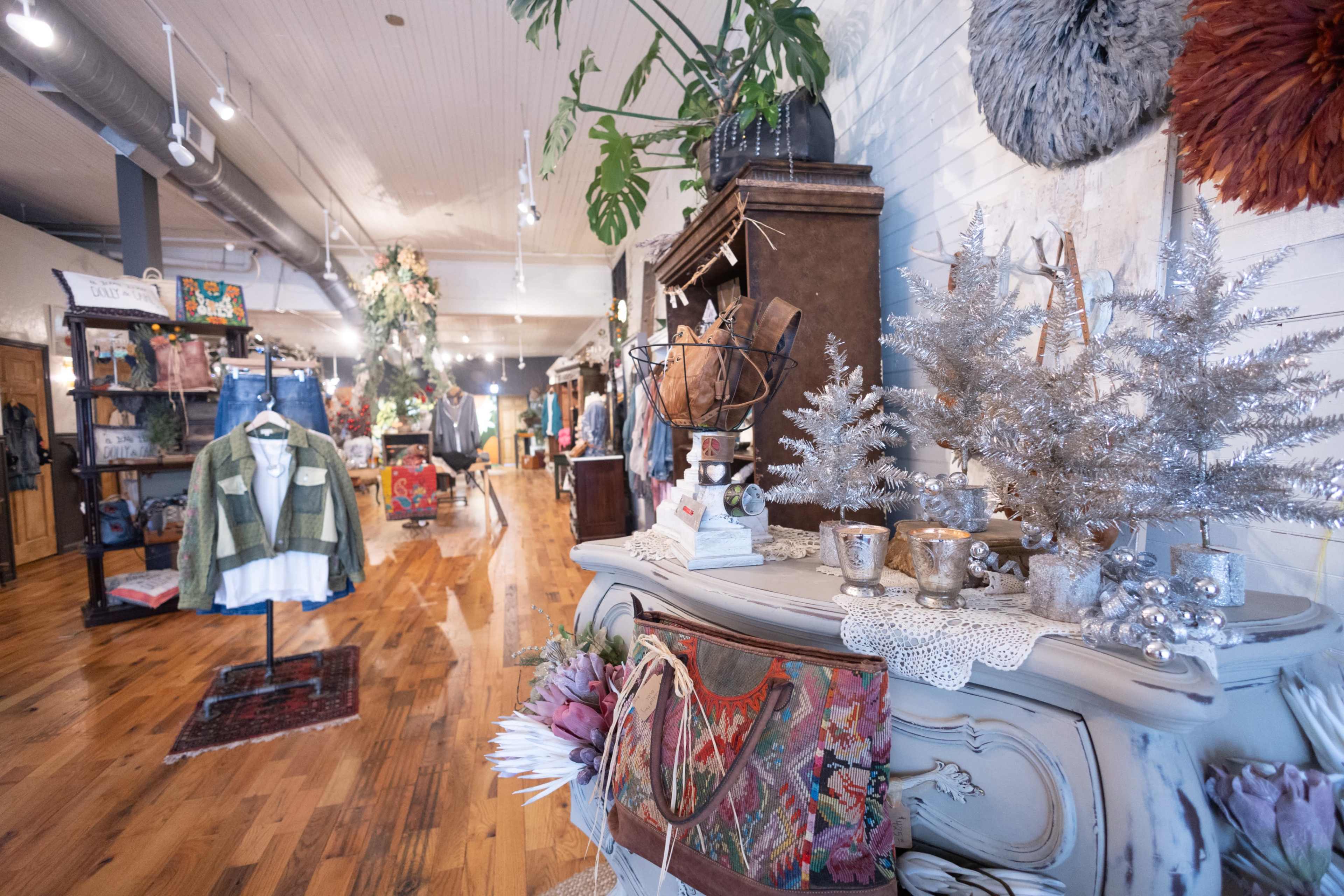 The image shows an interior of a boutique featuring clothing displays, decorative items, and a wooden floor.