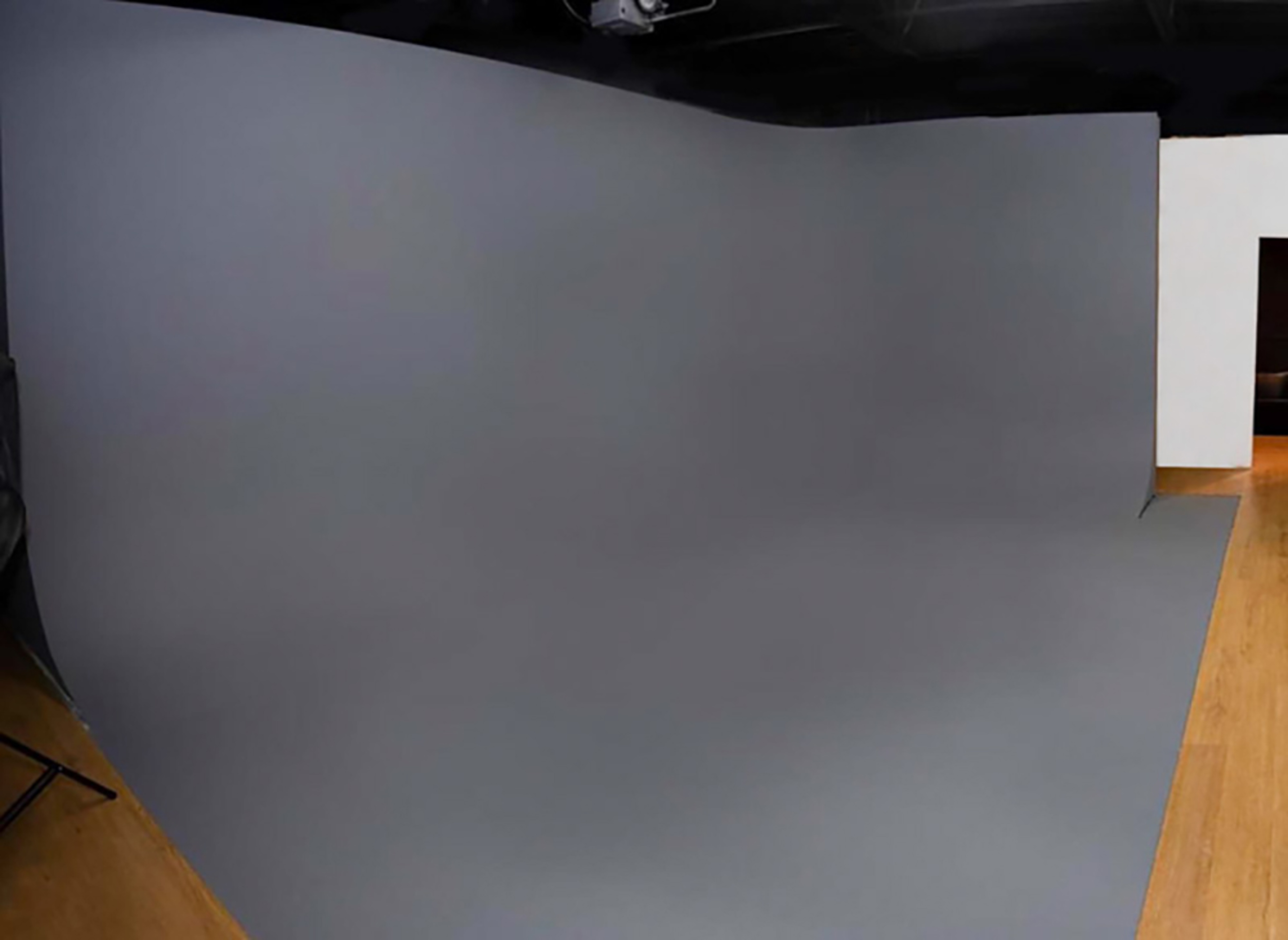 A spacious studio with a smooth gray backdrop and wooden flooring.