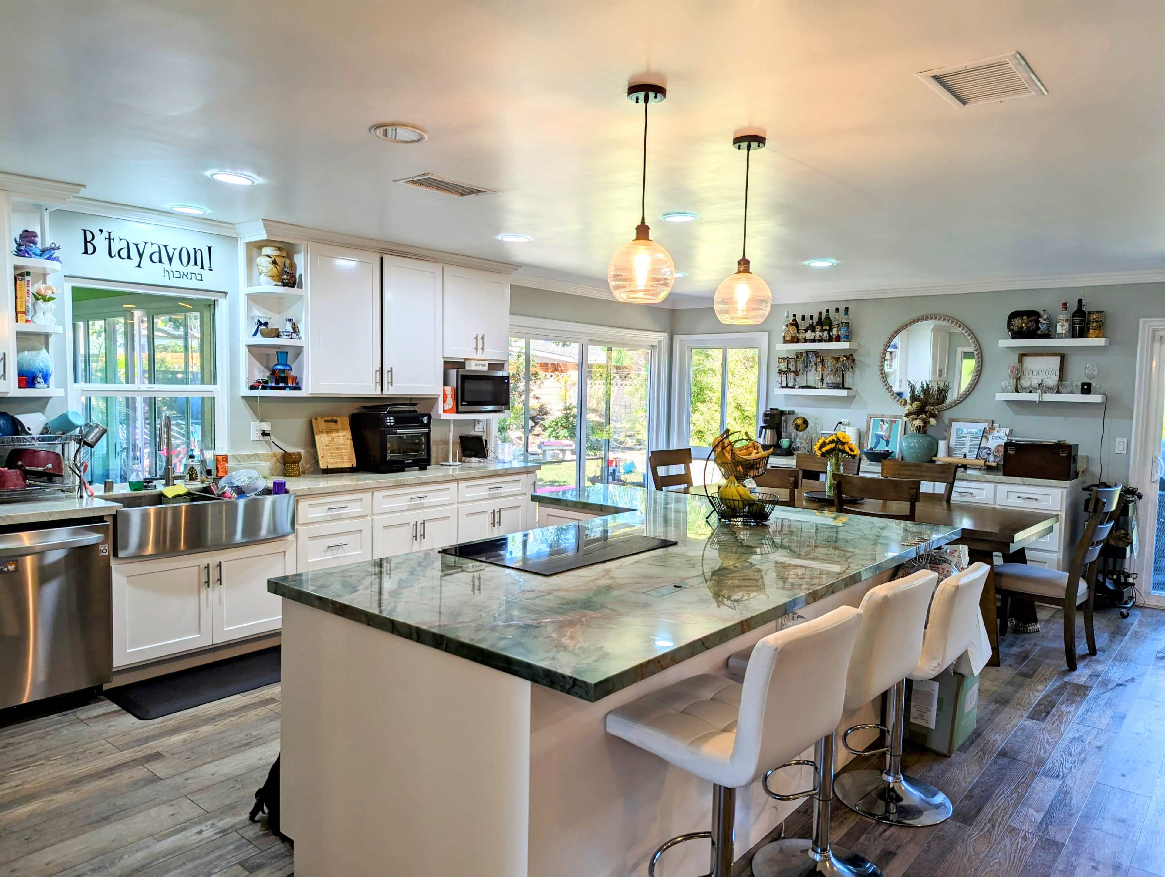 The kitchen features a large island with a marble countertop, modern bar stools, and an array of windows allowing natural light to fill the space.