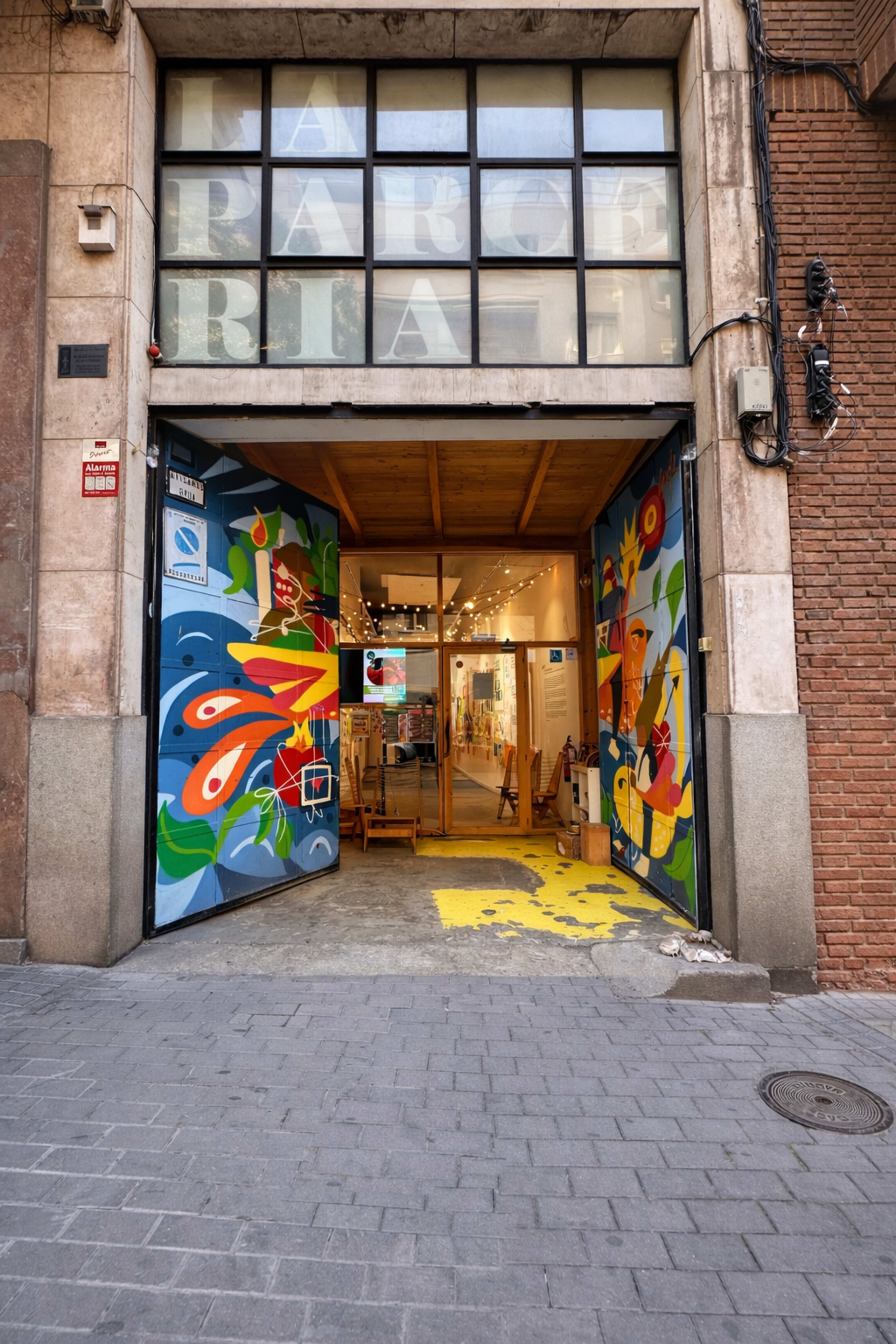 The image shows an open entrance to an art gallery, featuring colorful murals on the doors and a well-lit interior with artwork on display.