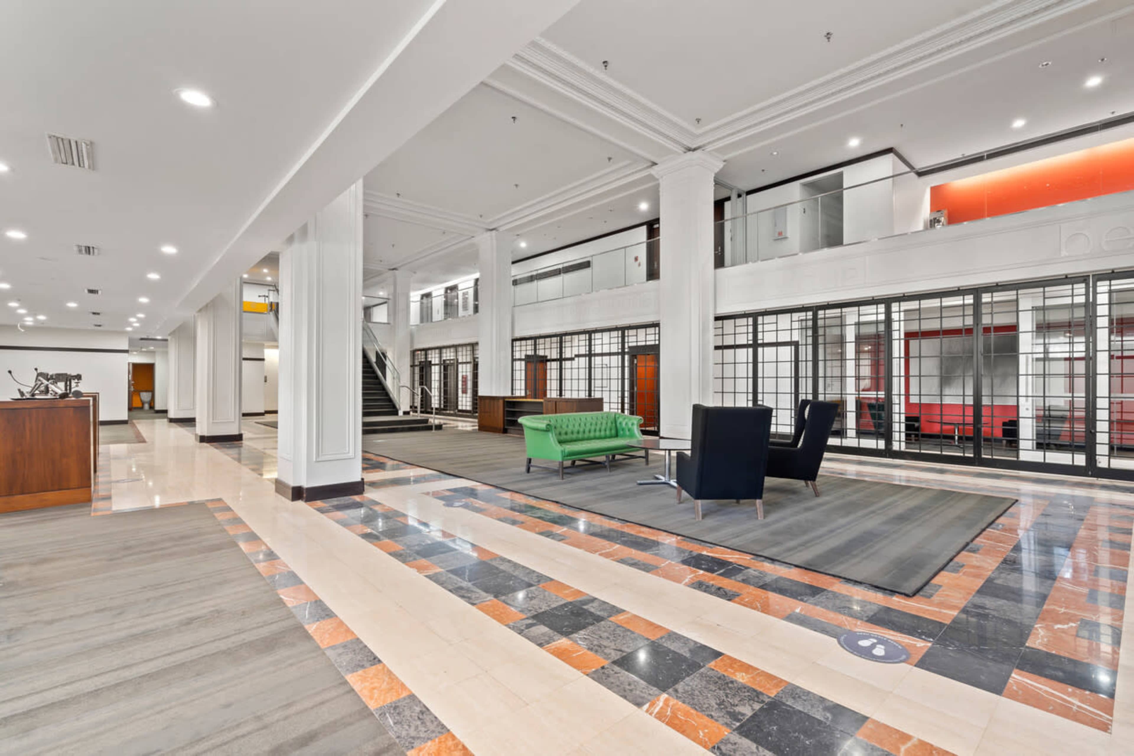 A spacious lobby area with a green sofa and a dark chair, framed by large windows and polished stone flooring.