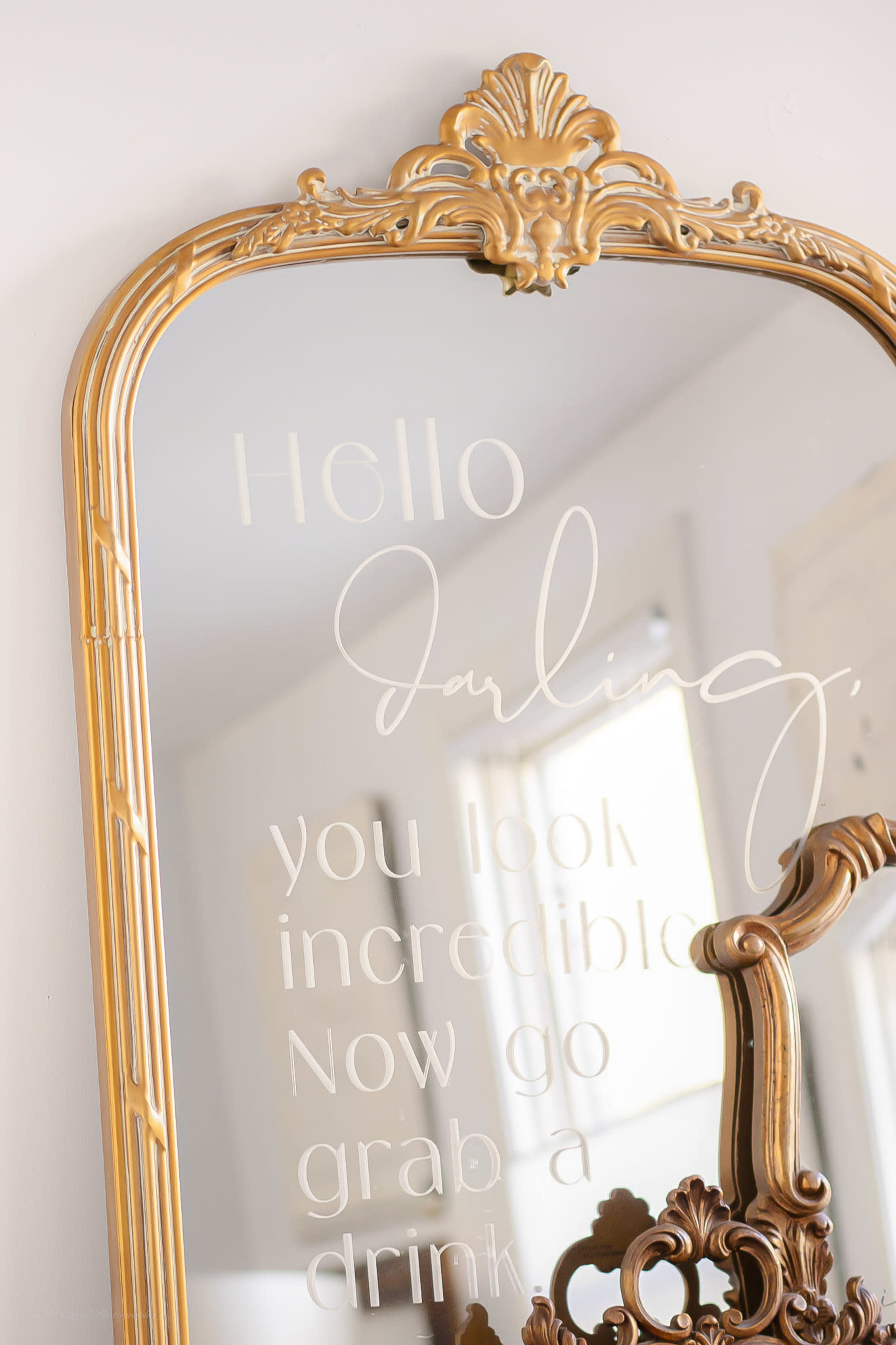A decorative gold-framed mirror features an inscription that reads, "Hello darling, you look incredible. Now go grab a drink."