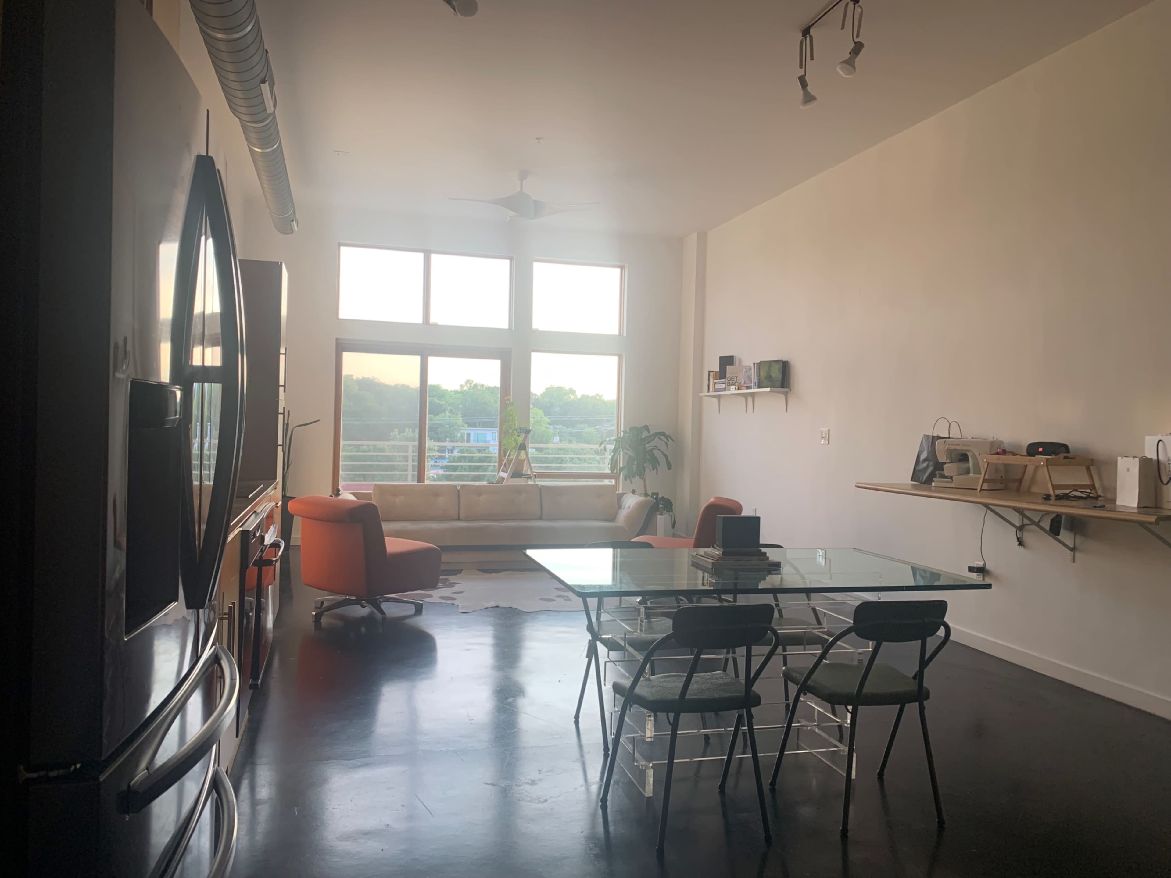 A modern, open-concept living space features large windows, a glass dining table, and a couch with an orange chair nearby.