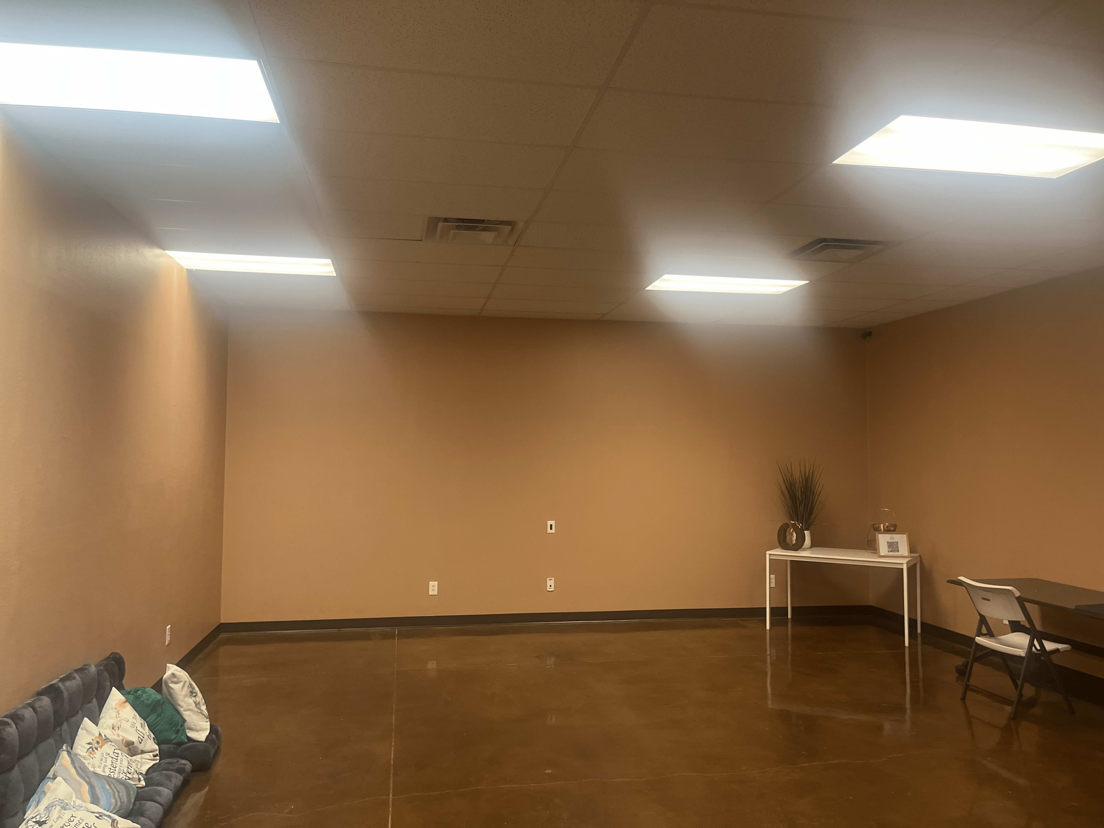An empty room with a polished concrete floor, light brown walls, and overhead fluorescent lighting.