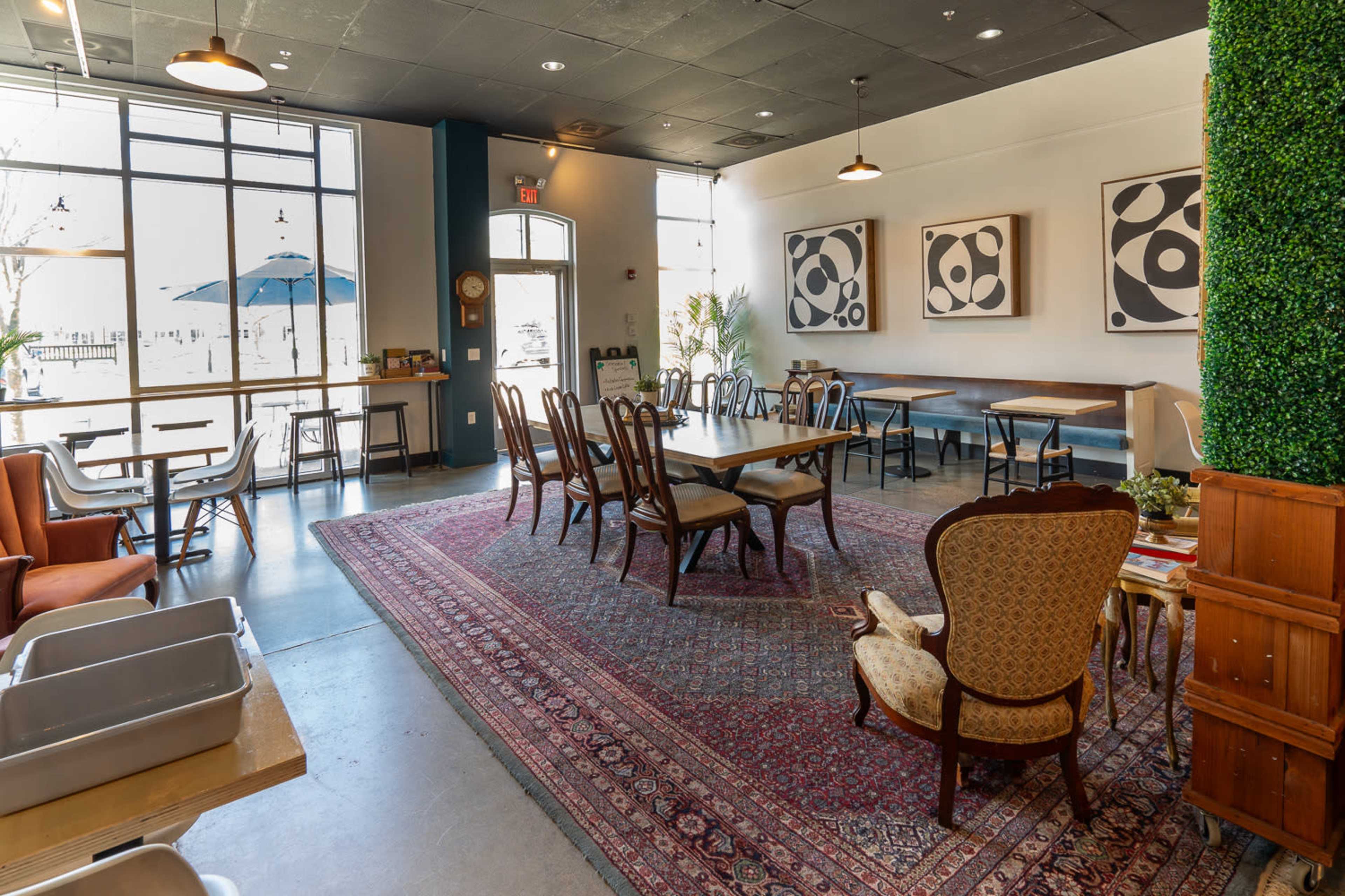 The interior of a café features a combination of wooden tables and chairs, an area rug, and framed artwork on the walls.