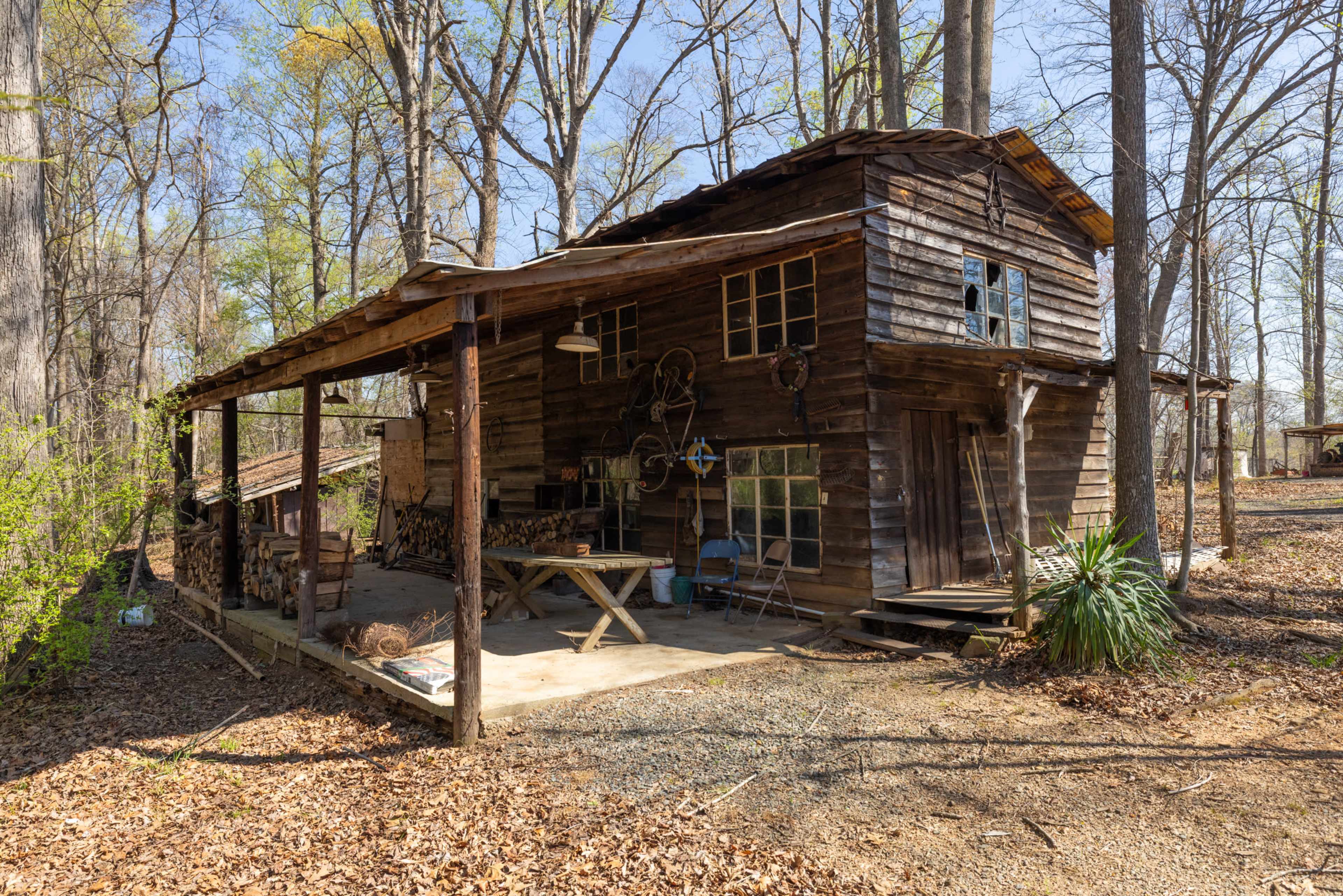 The image shows a rustic wooden cabin with a porch, surrounded by trees and fallen leaves.