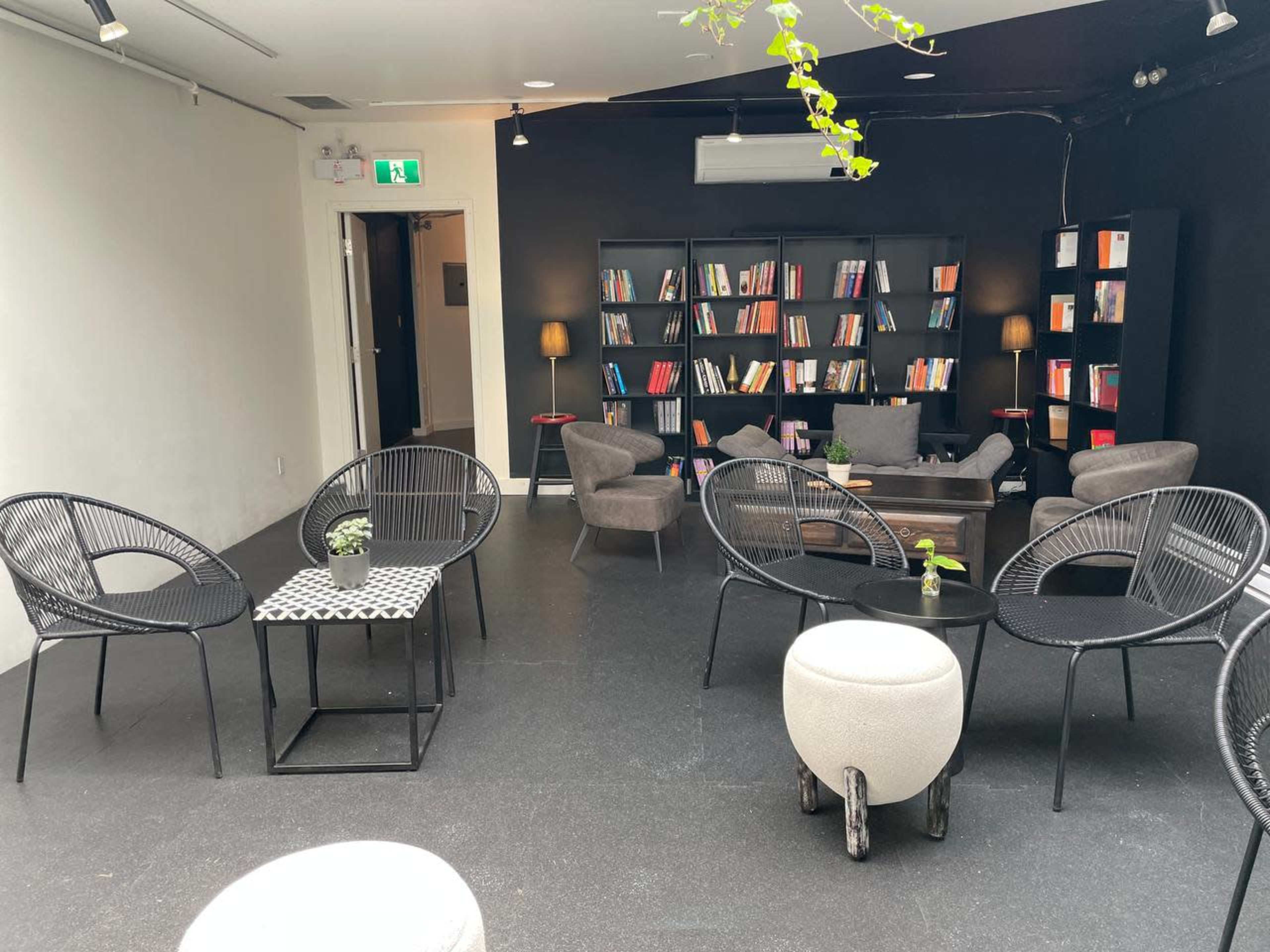 A minimalist lounge area with several chairs, a coffee table, and a bookshelf filled with books against a black wall.
