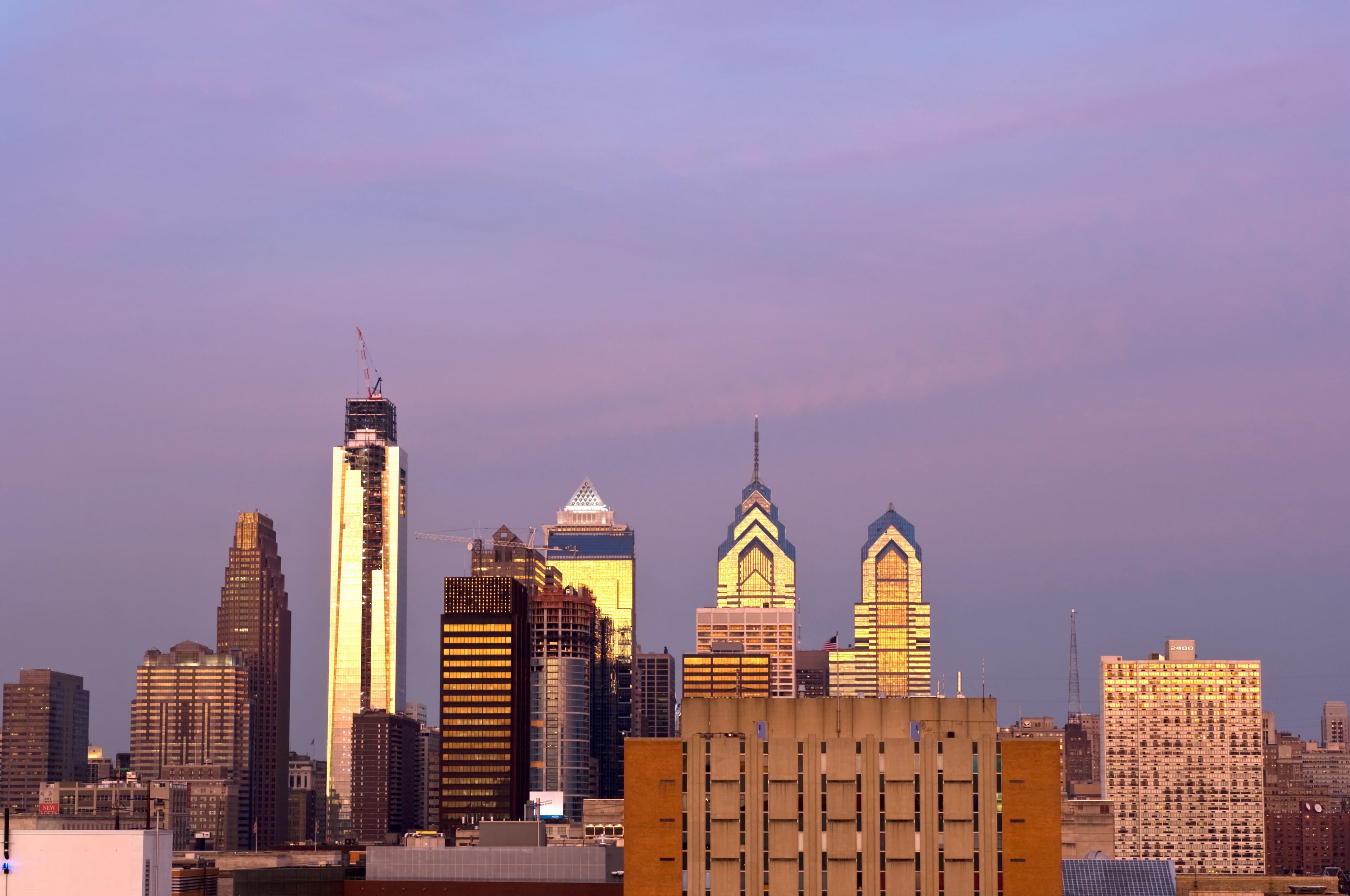 The skyline of Philadelphia is illuminated by the soft light of dawn, showcasing a mix of modern skyscrapers and historic architecture.