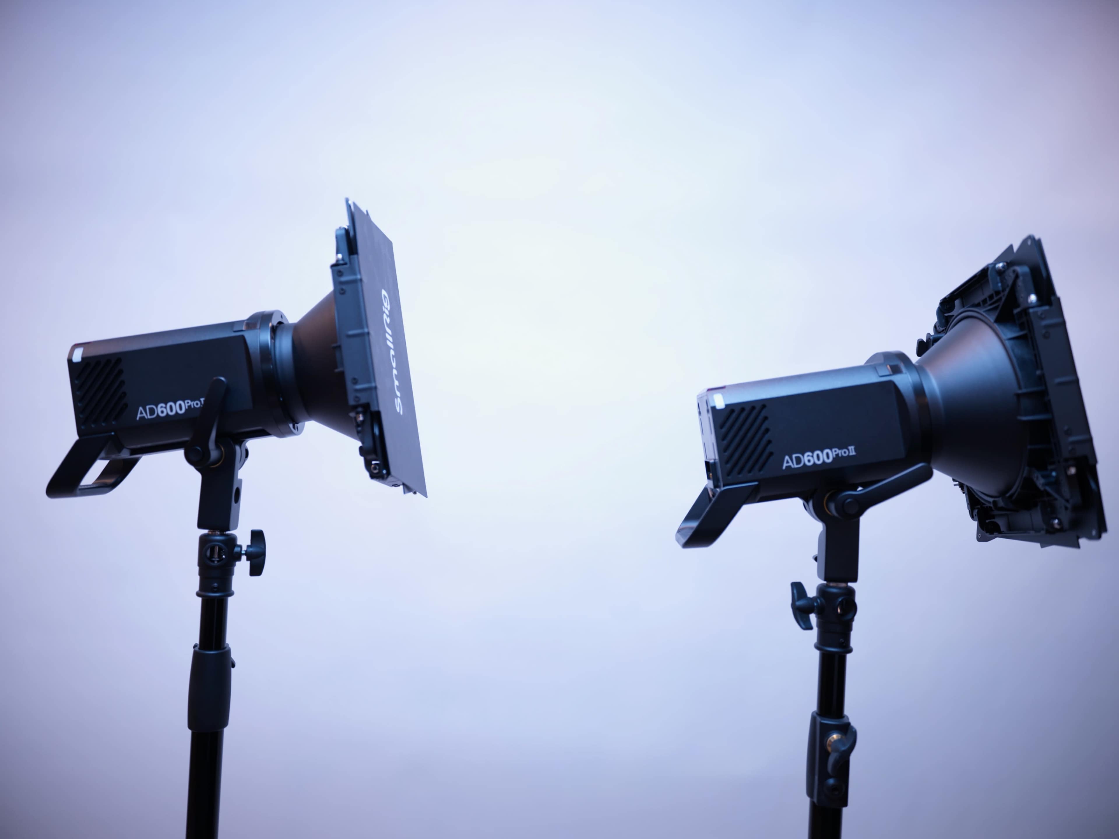 Two studio lights with softbox attachments are positioned on stands, facing each other against a neutral background.