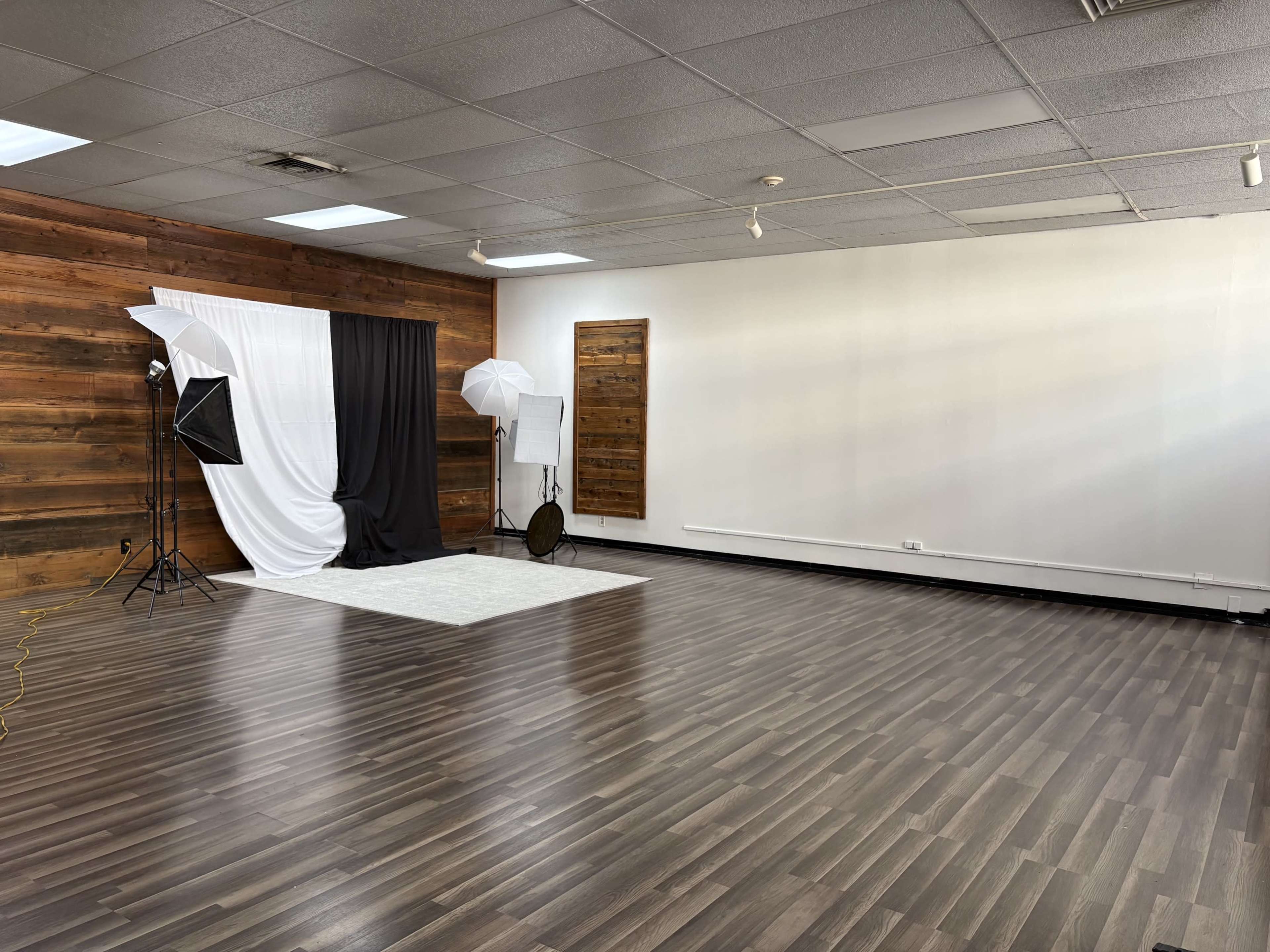 The image shows a spacious photography studio with wooden walls, a white and black backdrop, and two softbox lighting setups on stands.