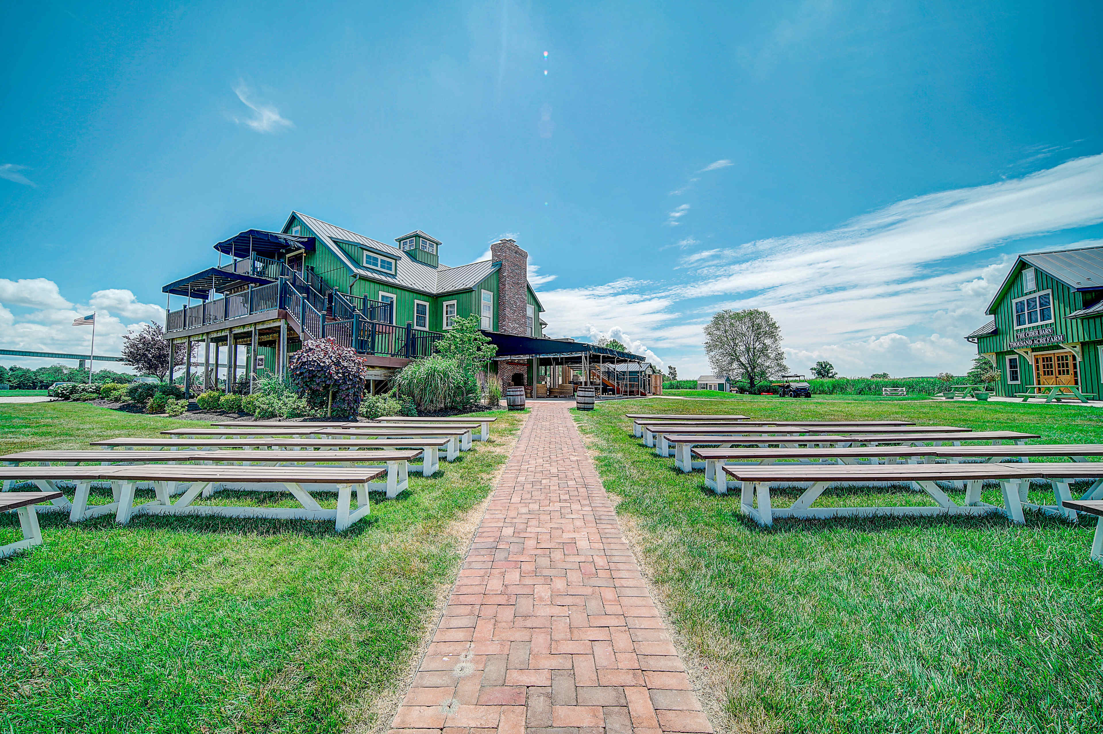 A brick path leads to a green building with multiple levels and outdoor seating surrounded by grassy areas and trees.