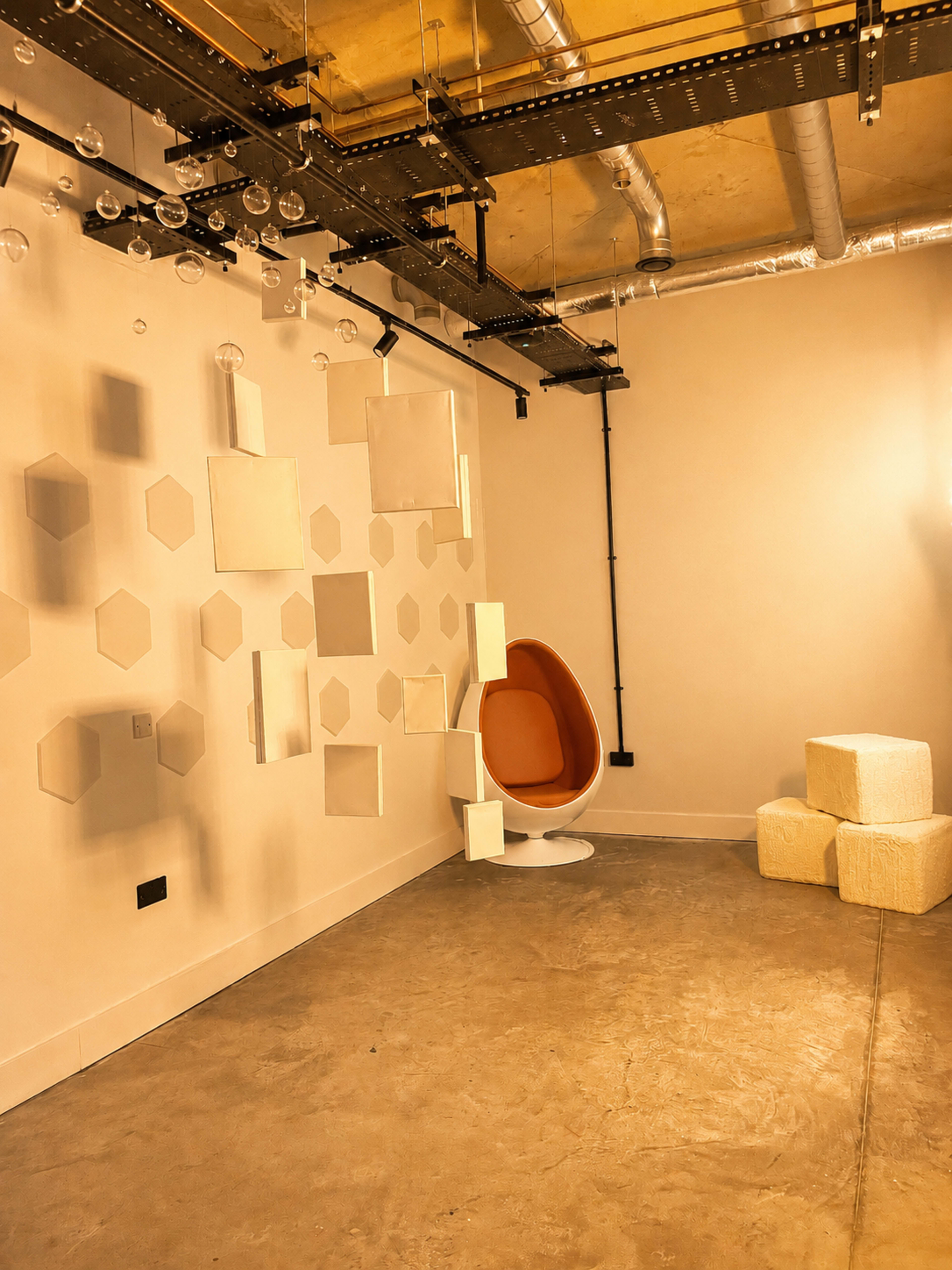 The image shows a modern interior space featuring an orange hanging chair, a few textured blocks, and a wall with hexagon-shaped decorations and mirrors.