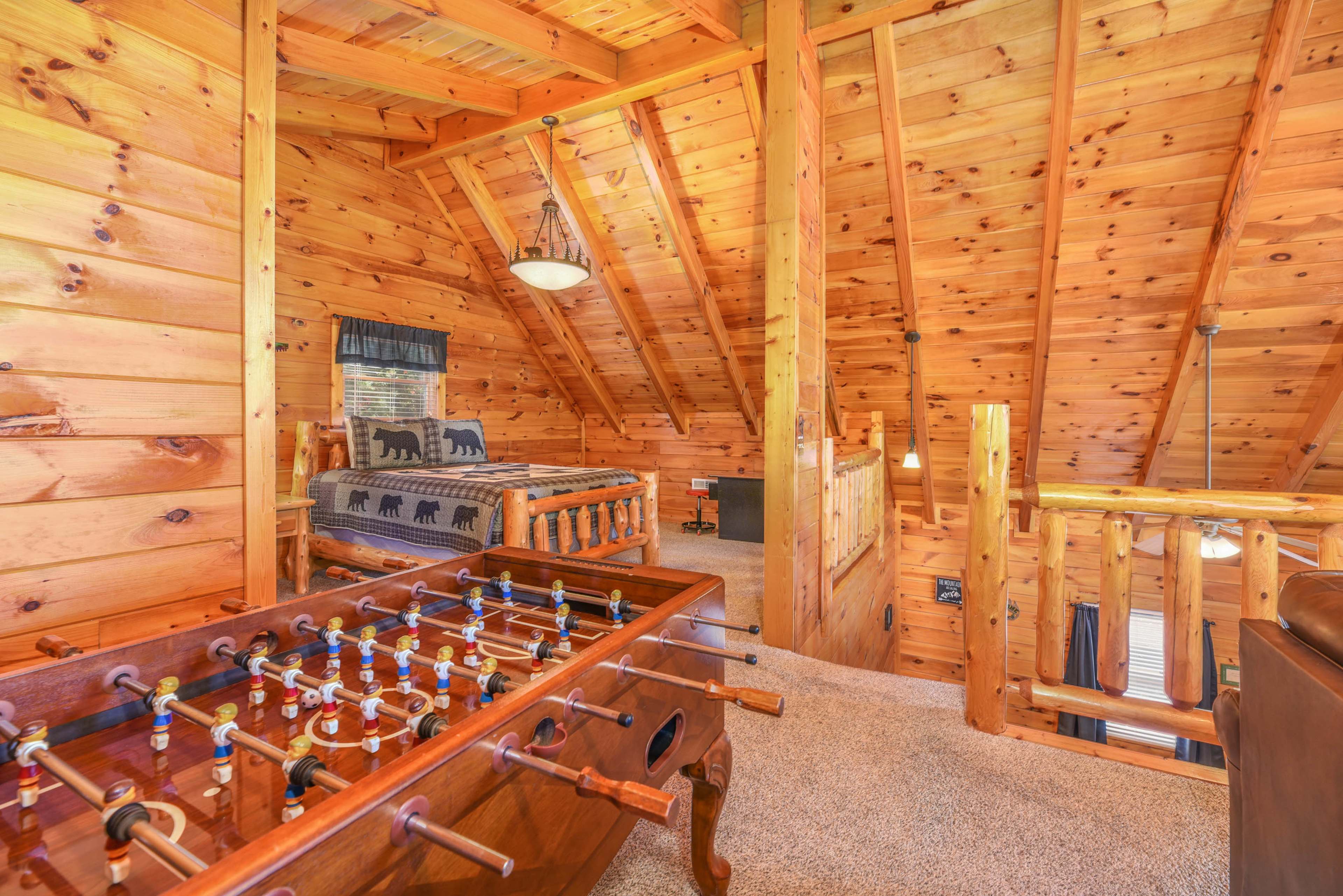 A loft area features a foosball table, a wooden bed, and a rustic pine wood ceiling.